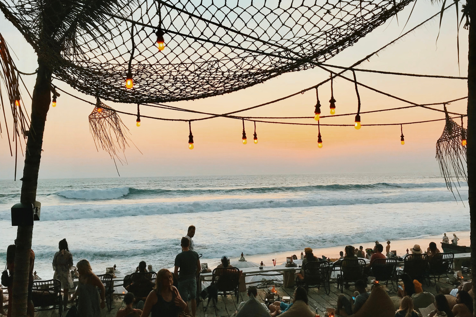 A group of people are sitting at tables on a beach at sunset.