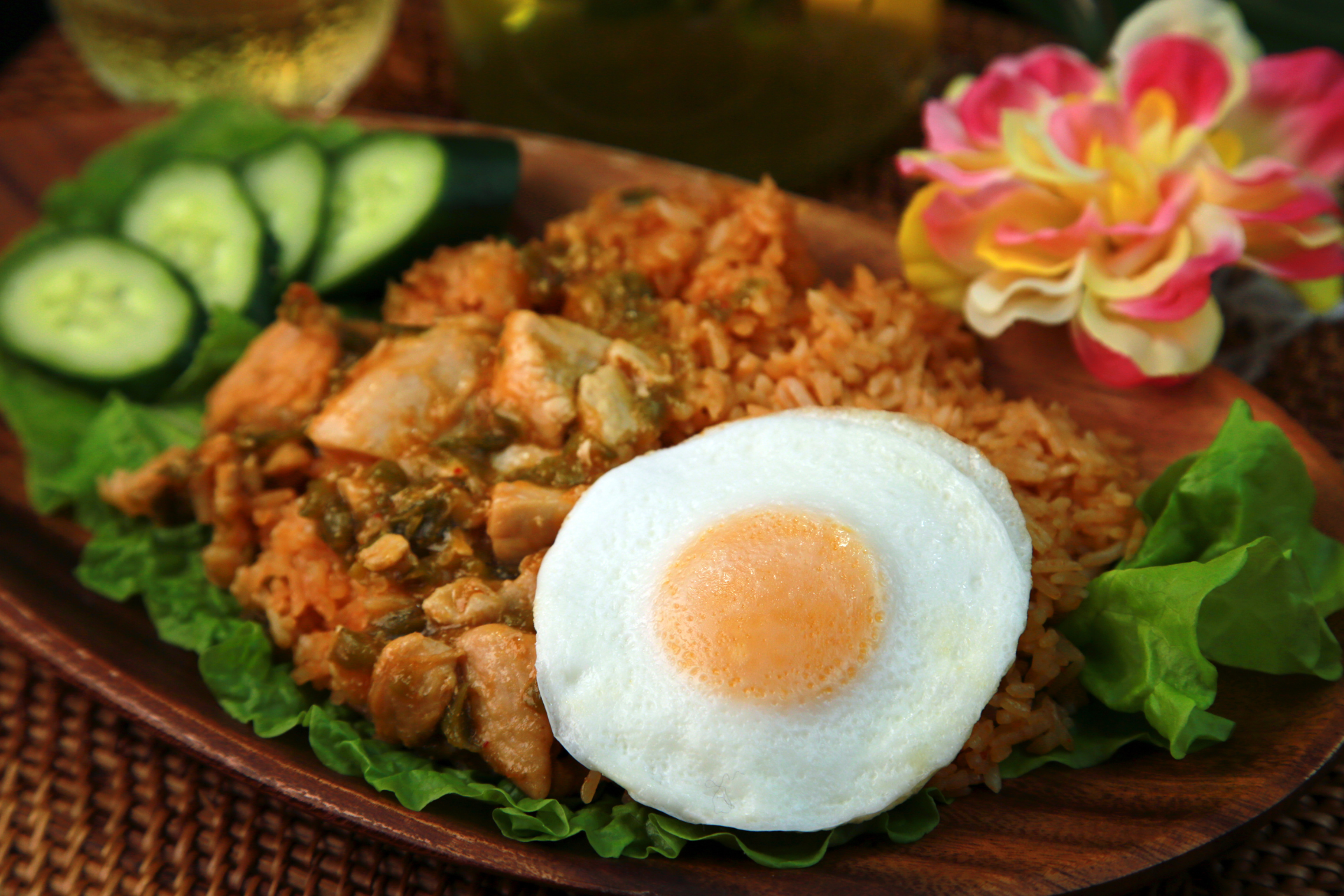 A wooden plate topped with rice , eggs , cucumbers and lettuce.