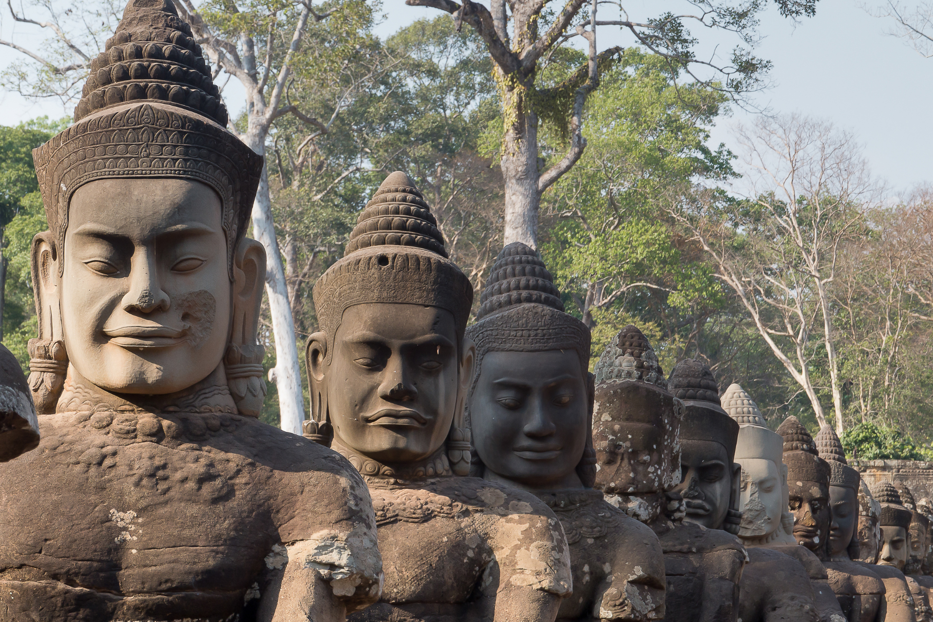 A group of statues are lined up in a row with trees in the background