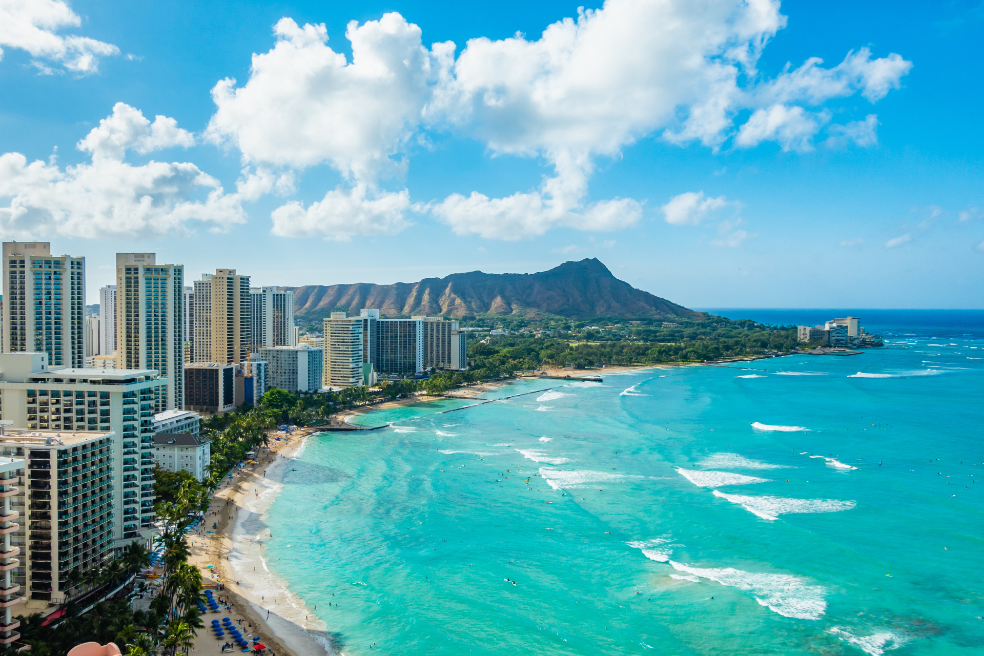 An aerial view of a beach in hawaii with a mountain in the background.