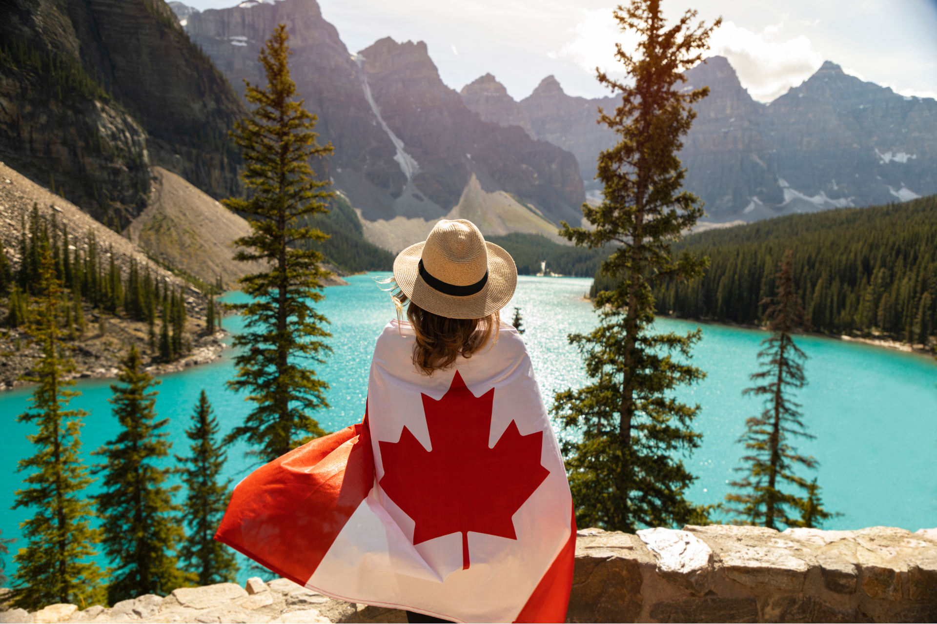A woman wrapped in a canadian flag is looking at a lake.