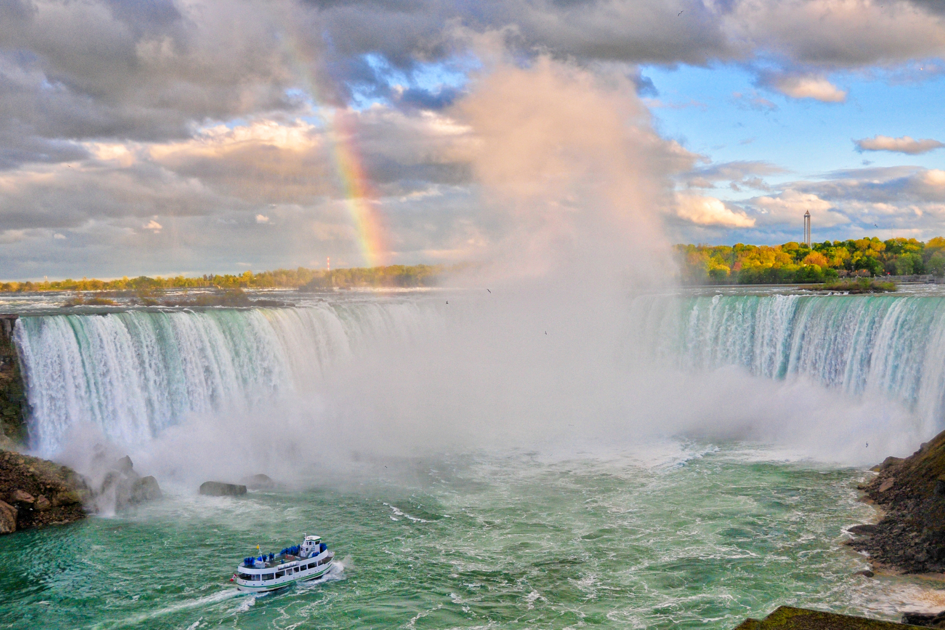 A boat is going down a waterfall with a rainbow in the background.