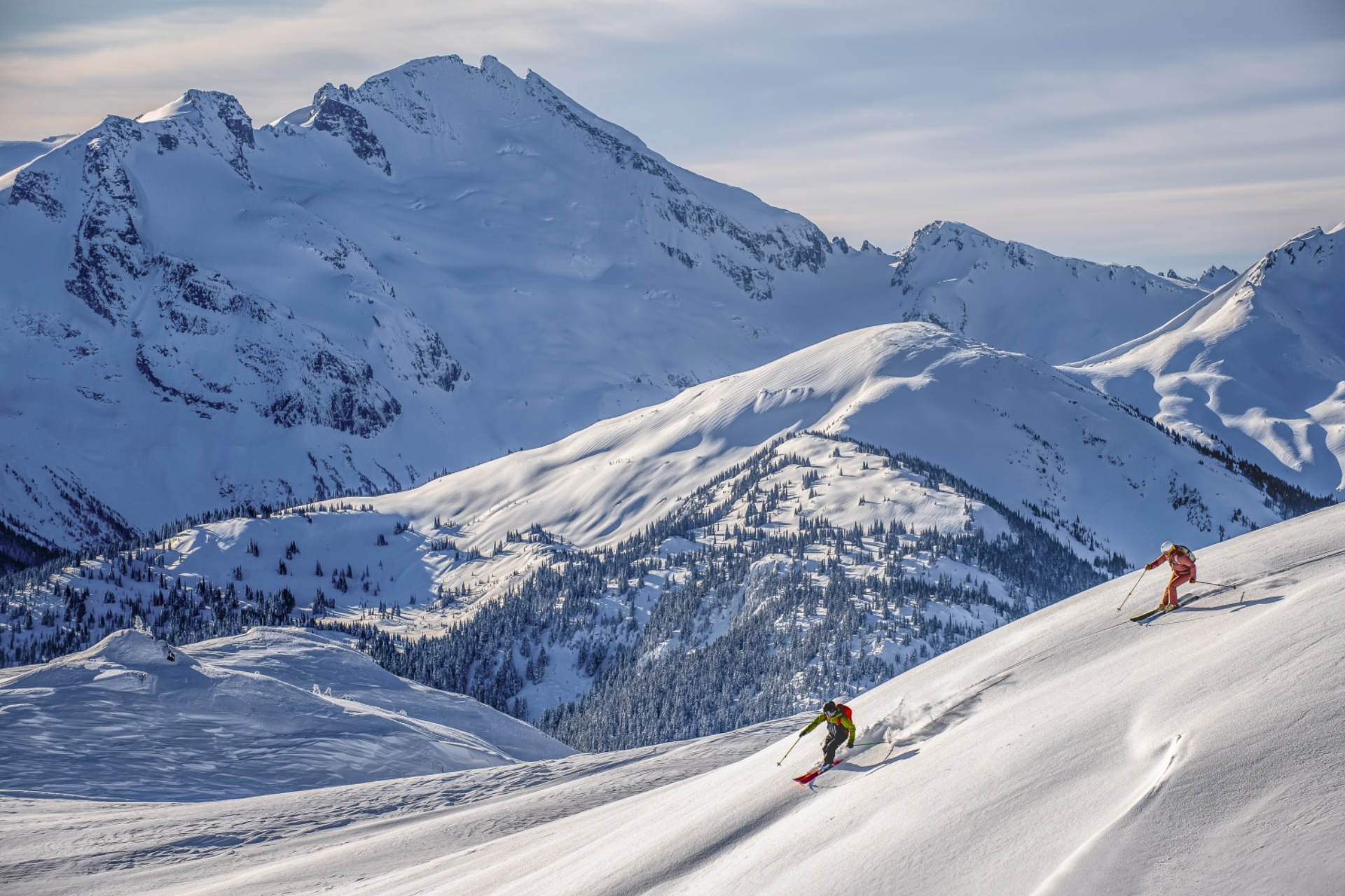 Two people are skiing down a snow covered mountain.