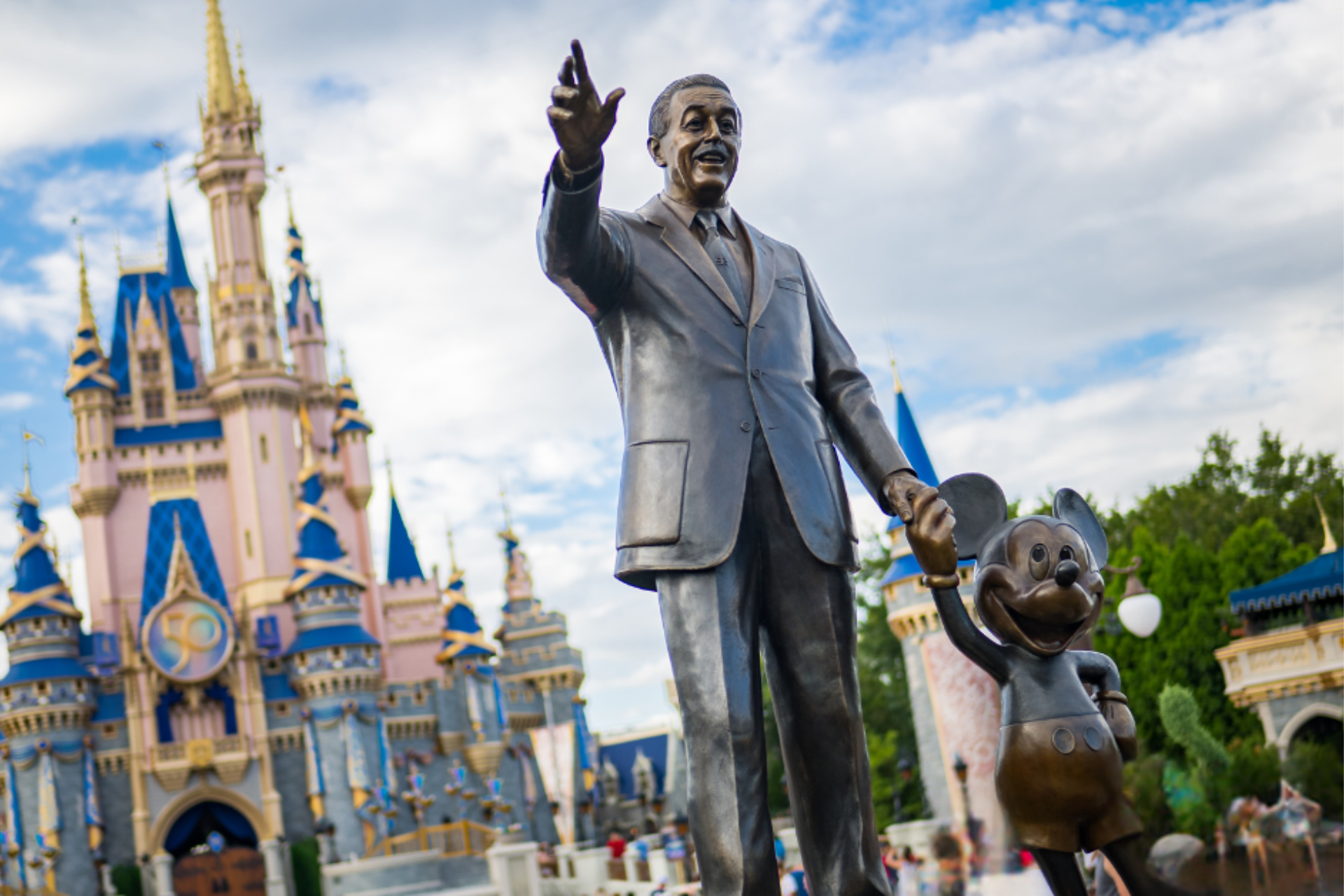 A statue of walt disney and mickey mouse in front of a castle.
