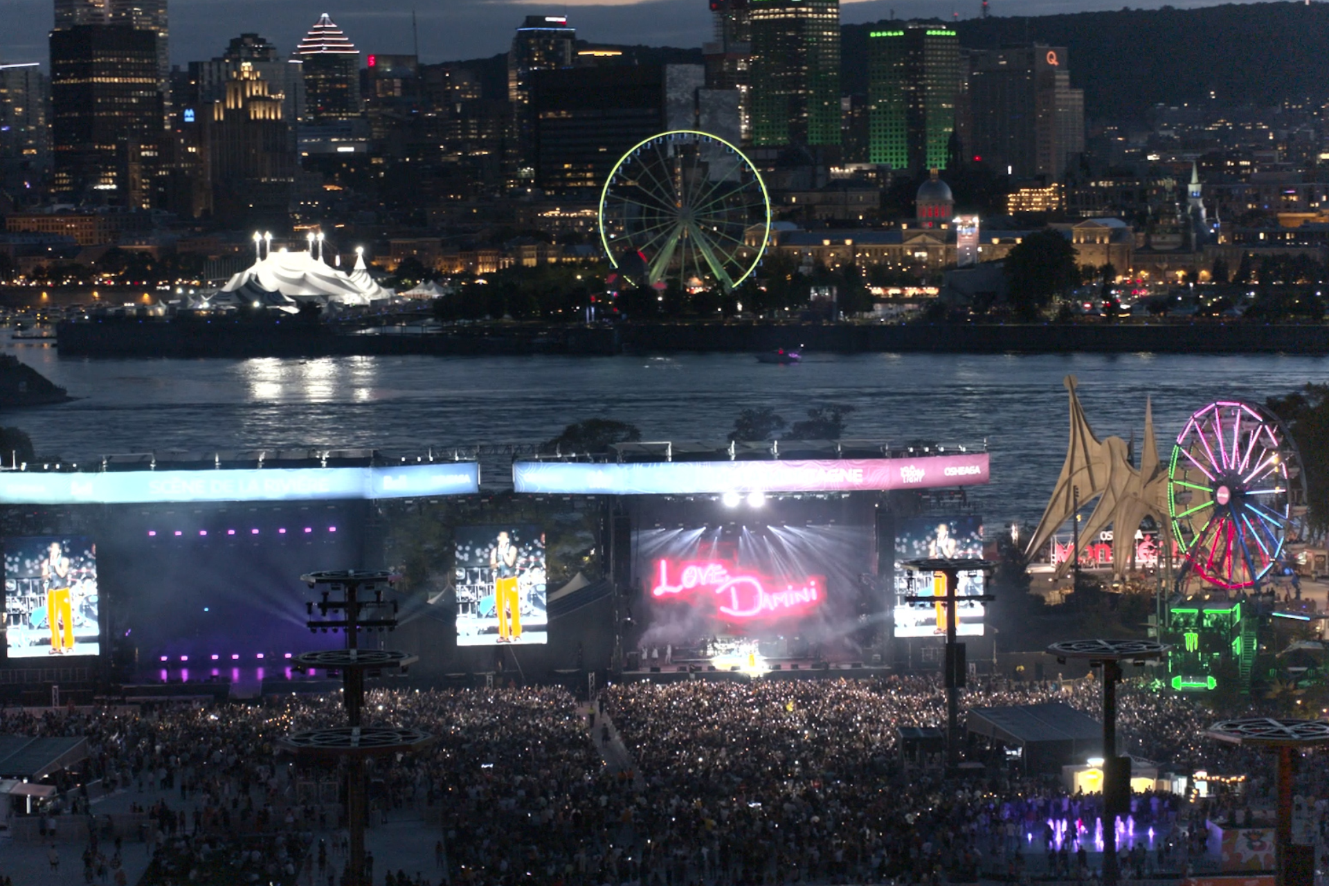 A large crowd is gathered at a concert with a ferris wheel in the background