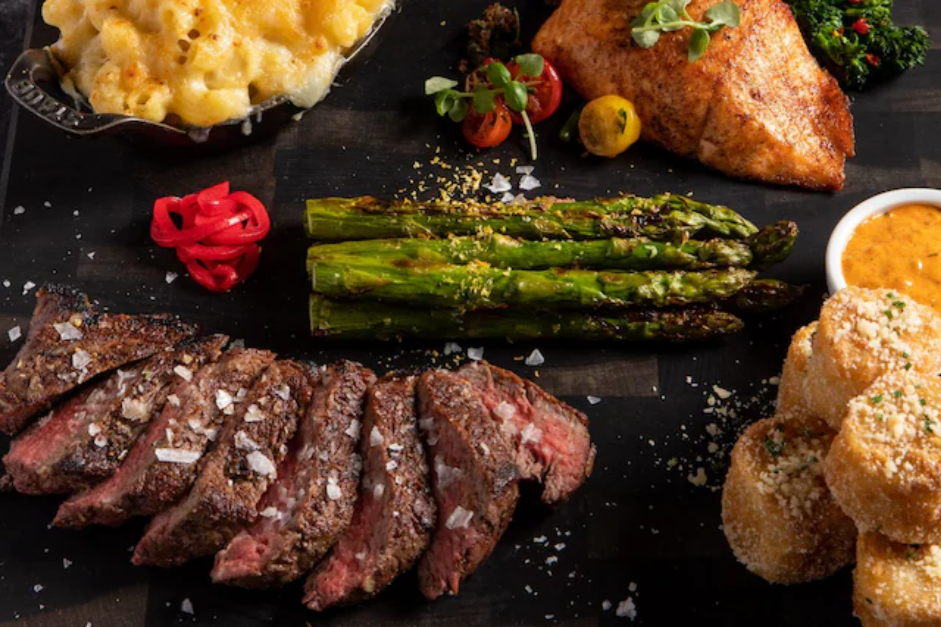 A plate of food with steak , asparagus , macaroni and cheese , and fish on a table.