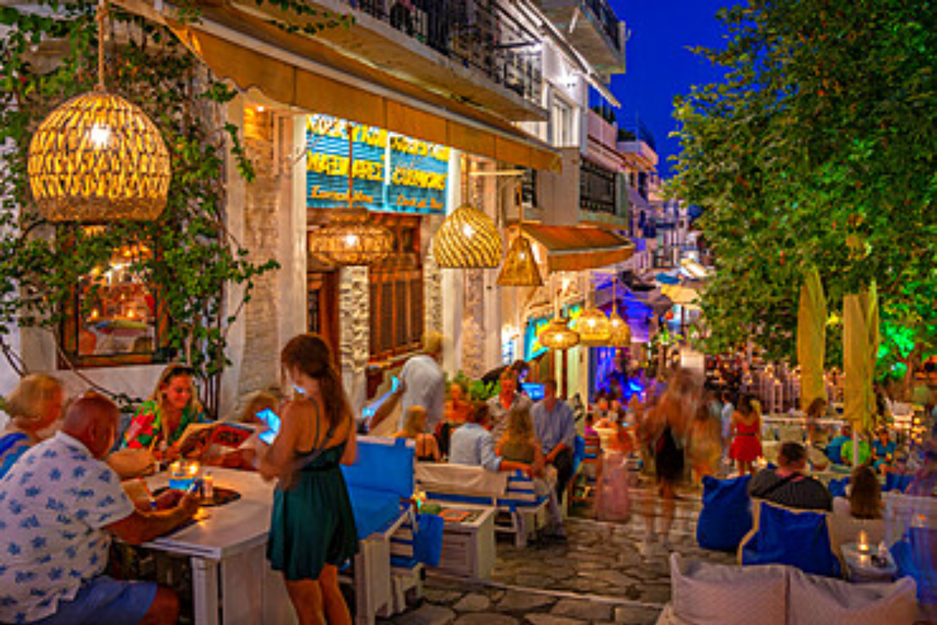 A group of people are sitting at tables outside of a restaurant at night.