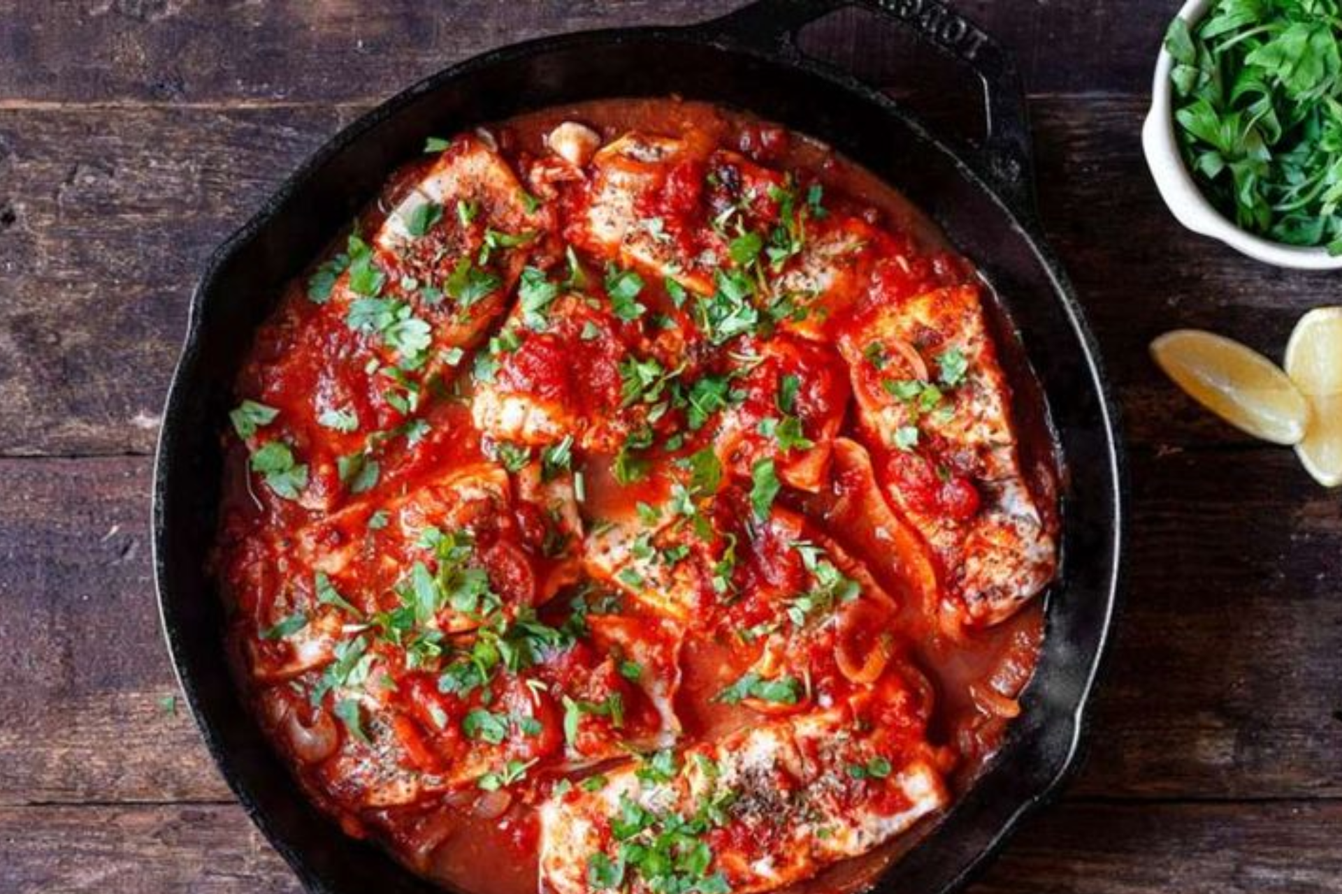 A skillet filled with meat and tomato sauce on a wooden table.