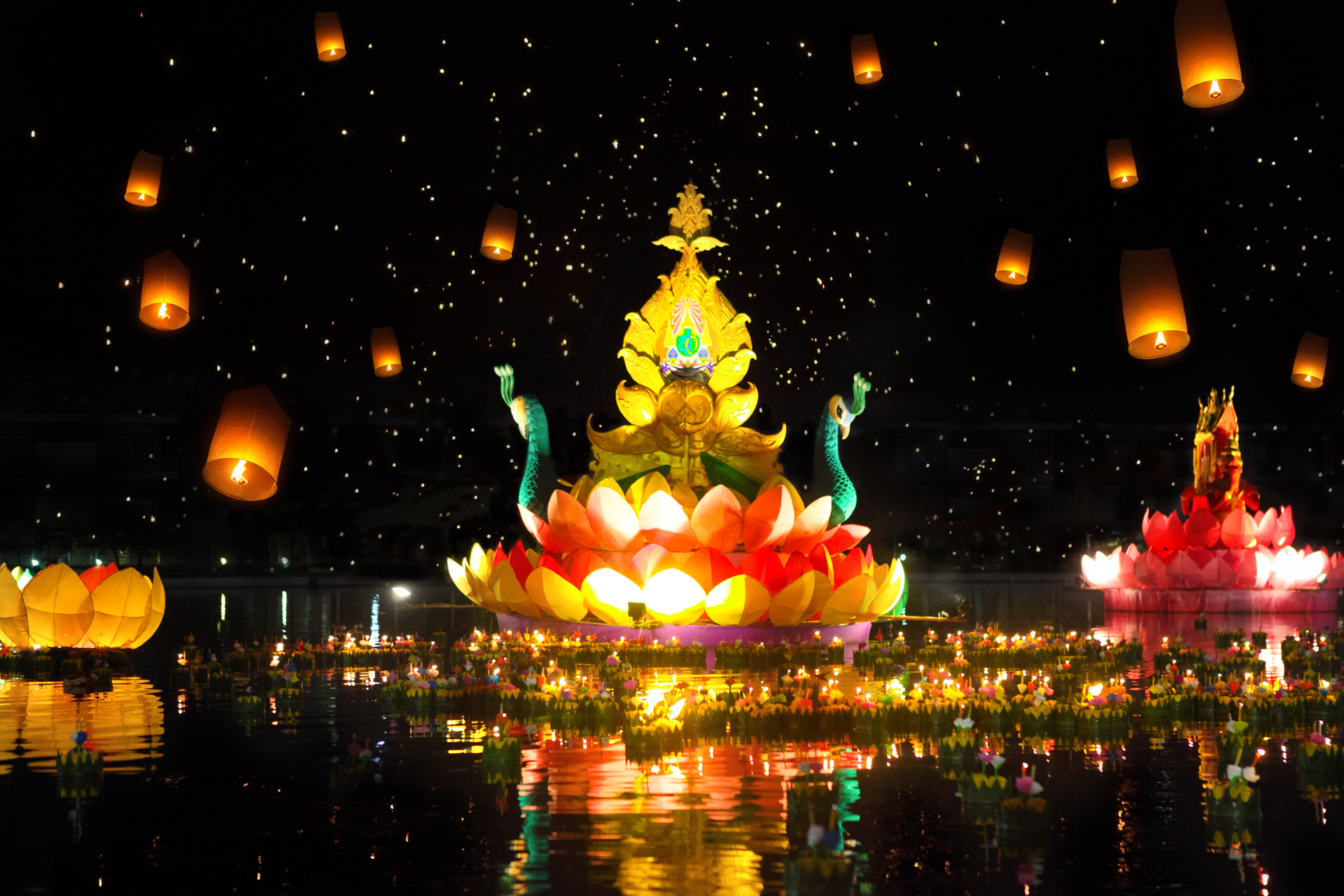 A lotus flower floating on top of a body of water with lanterns floating in the air.