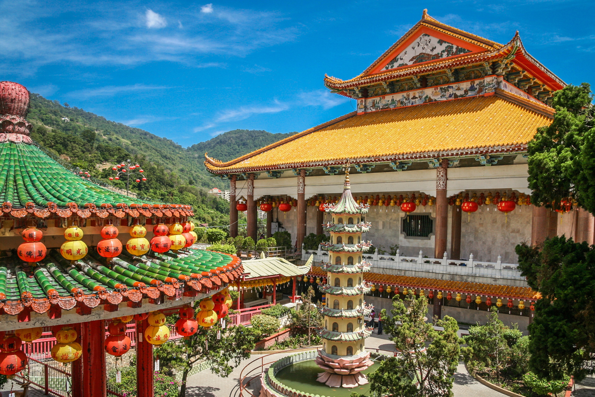 A large chinese building with a green roof is surrounded by trees and lanterns.