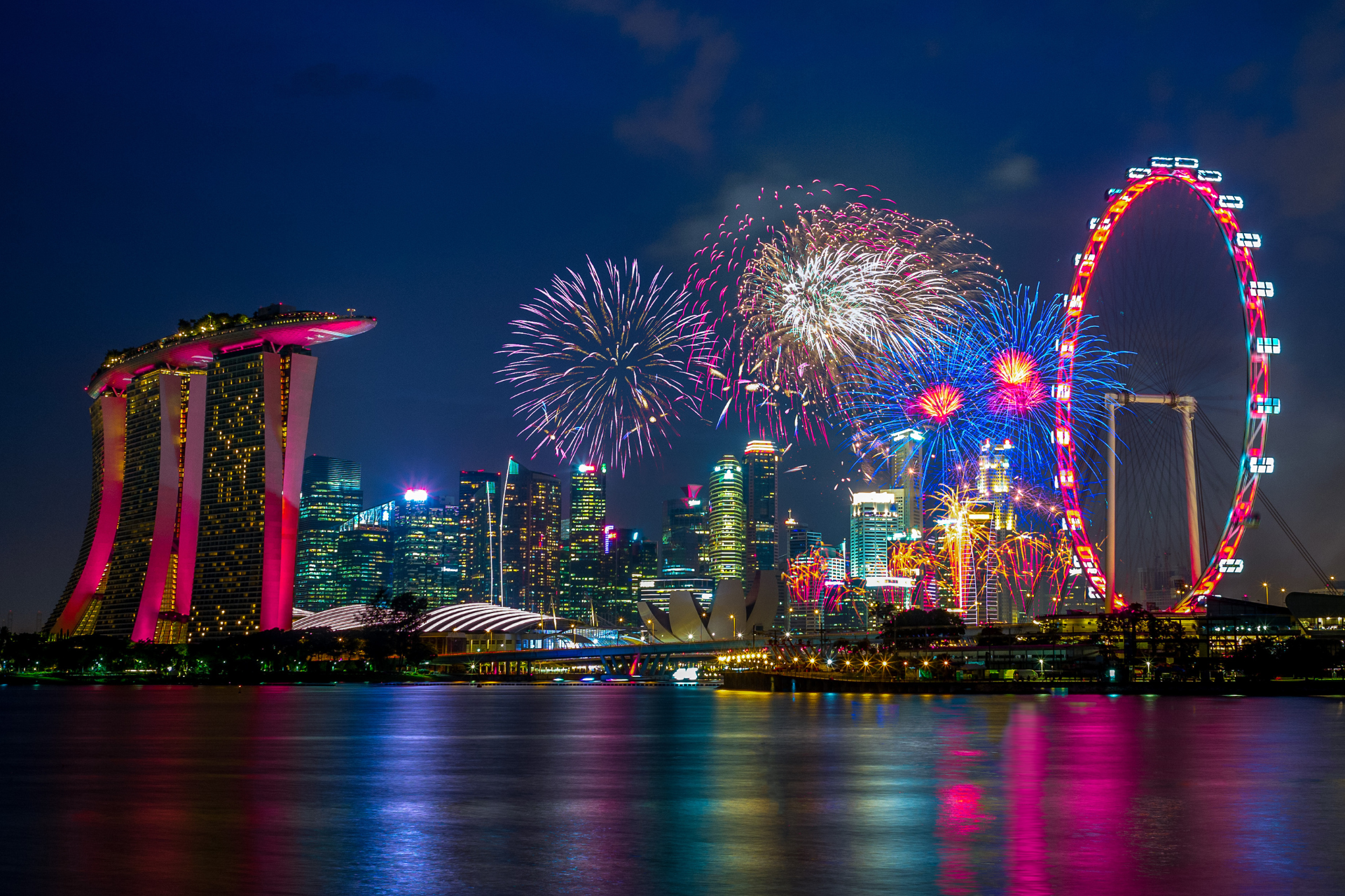 A city skyline with fireworks and a ferris wheel in the foreground.