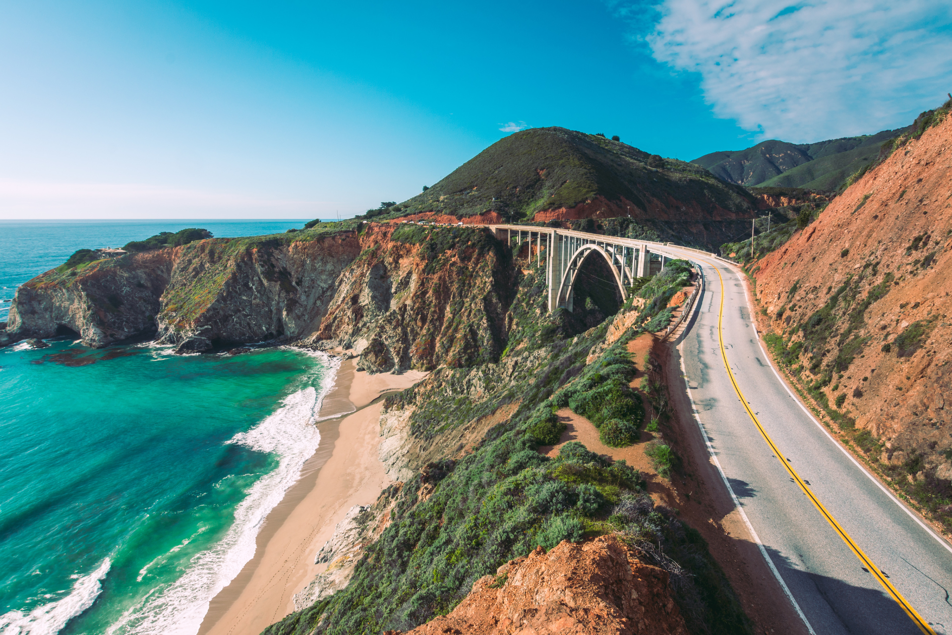 An aerial view of a highway going through a cliff overlooking the ocean.