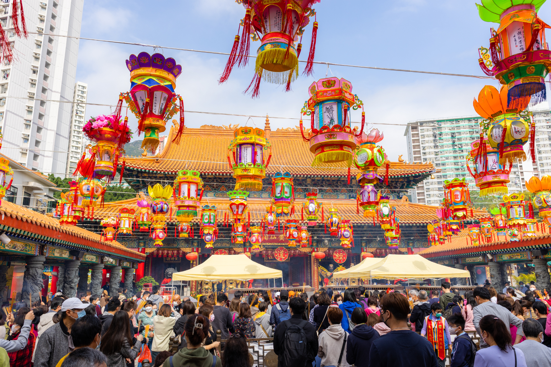 A crowd of people are walking in front of a temple decorated with lanterns.