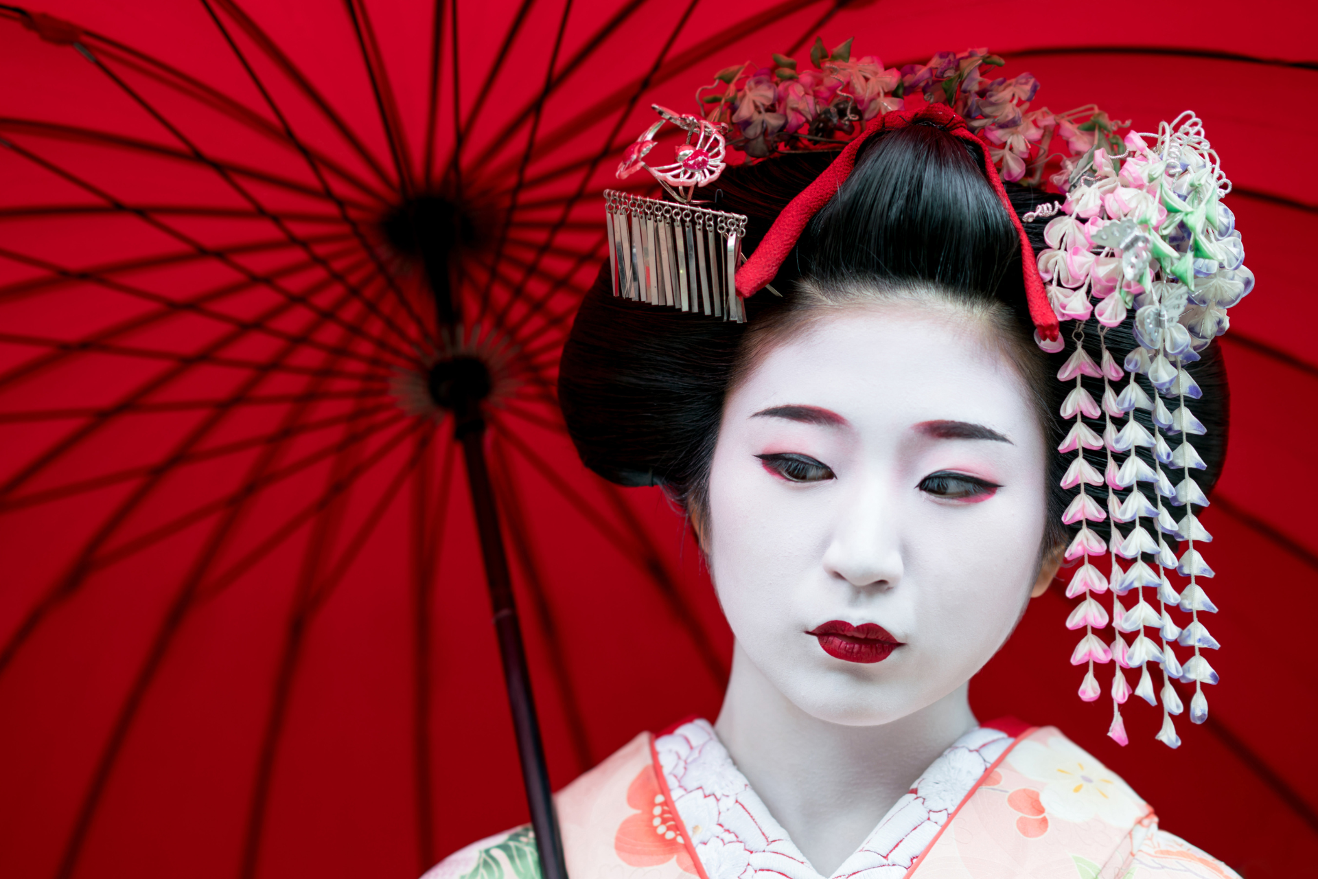 A geisha in a kimono is holding a red umbrella