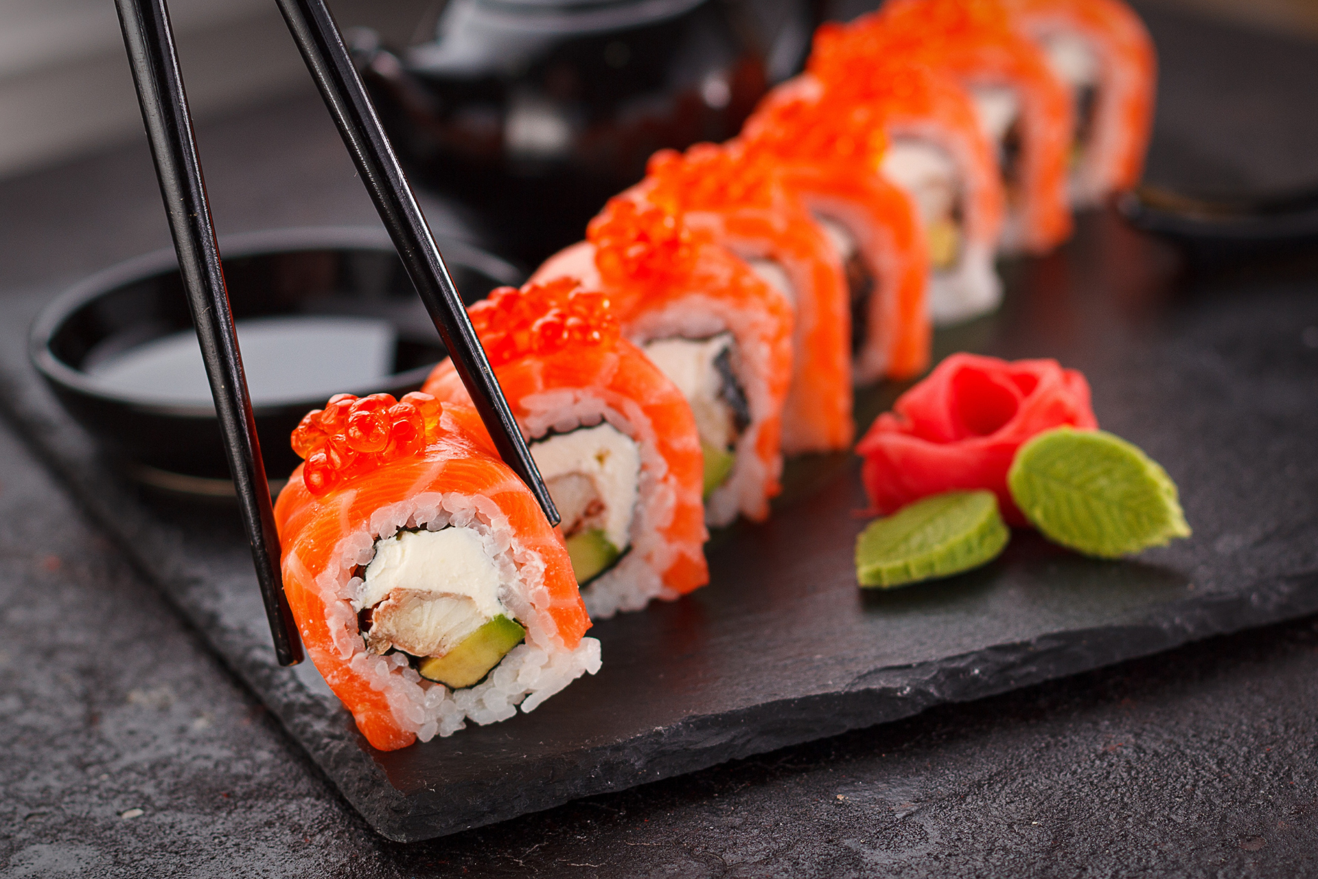 A person is taking a piece of sushi with chopsticks.