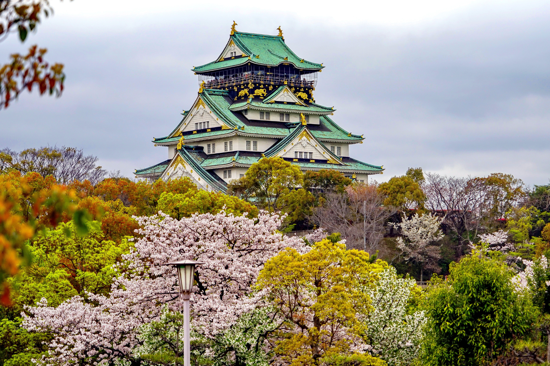 A castle with a green roof is surrounded by trees and flowers.