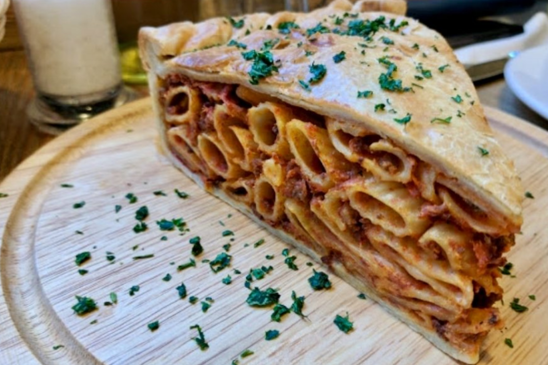 A slice of pasta pie is on a wooden cutting board.