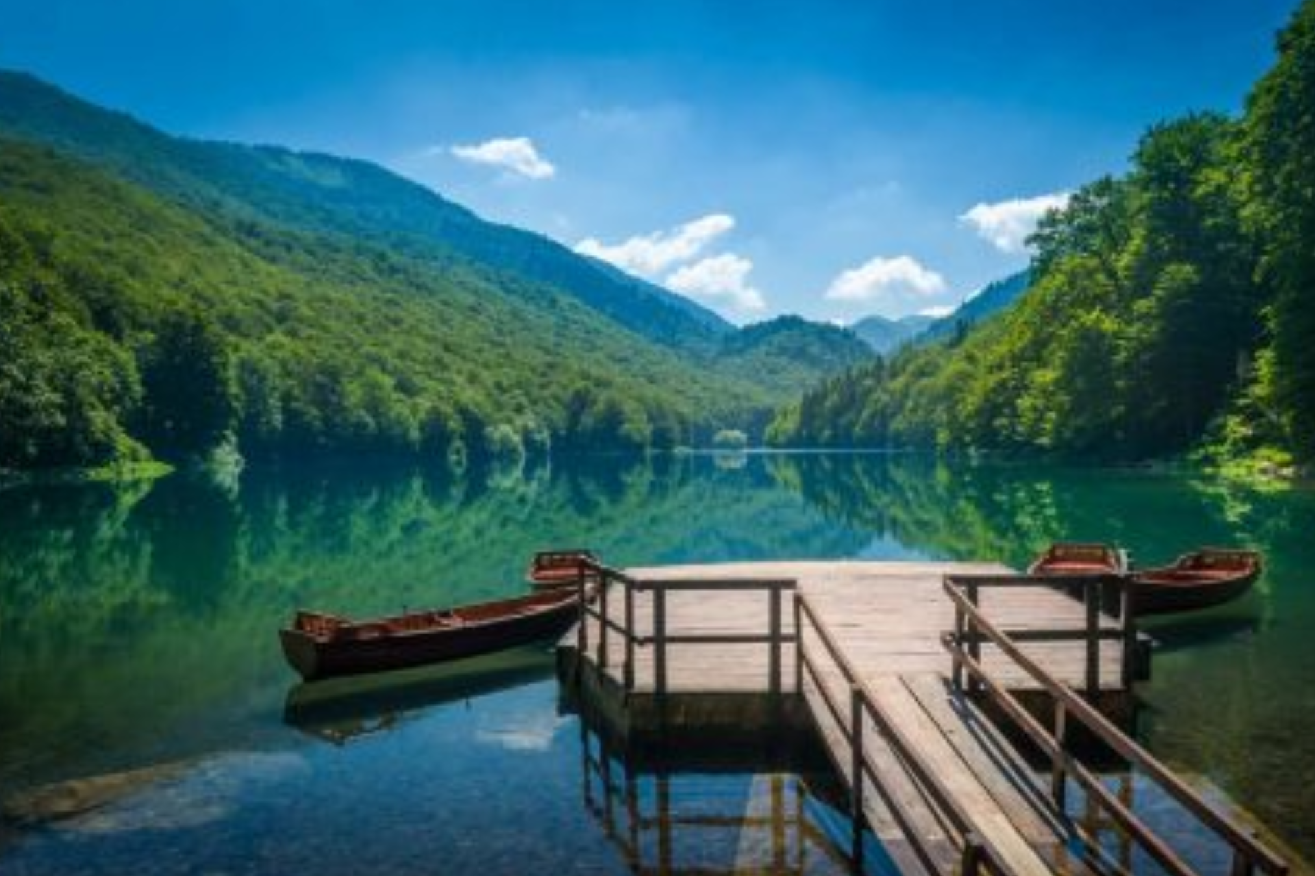 Two boats are docked at a dock on a lake surrounded by mountains.