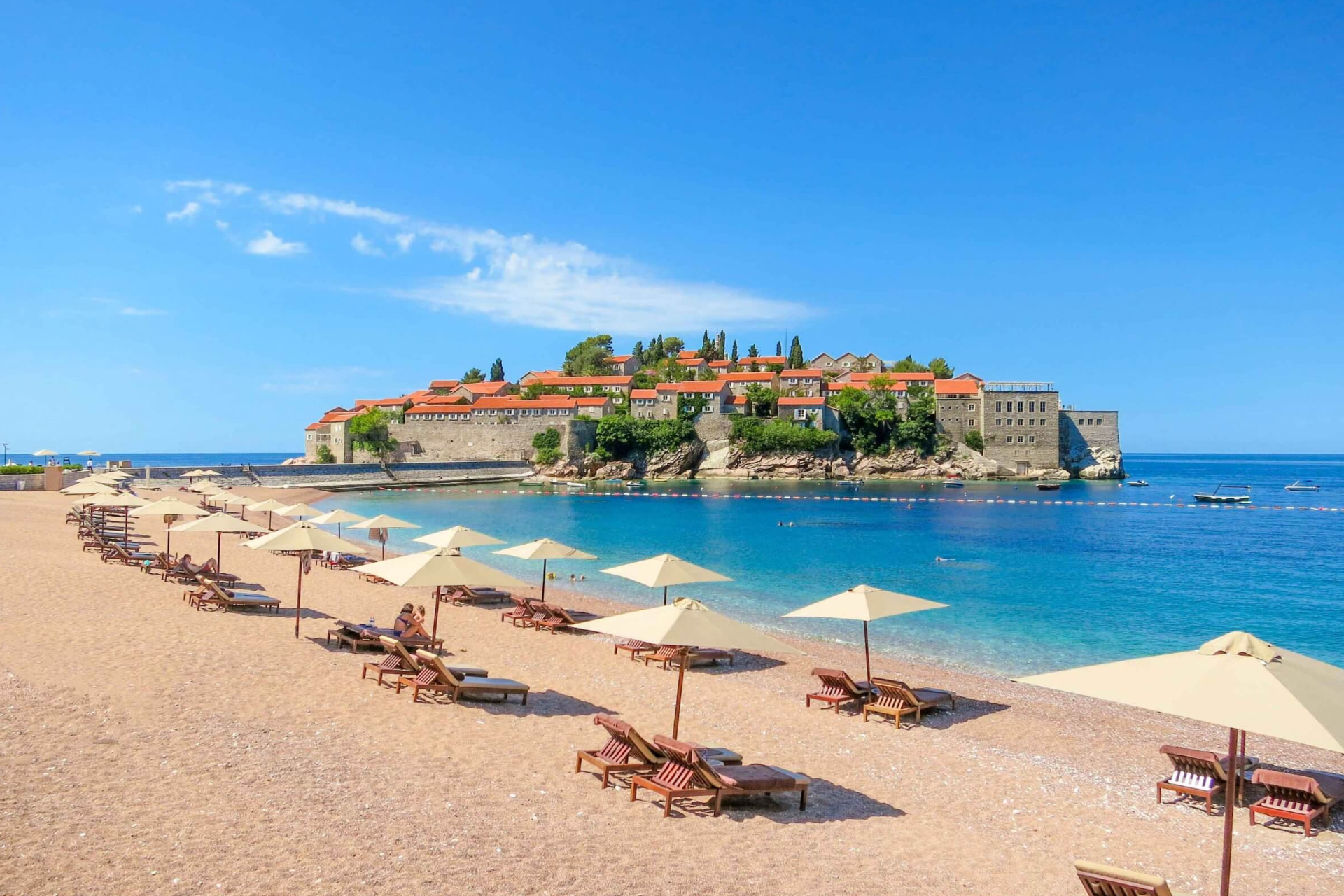 A beach with umbrellas and chairs and a small island in the background.