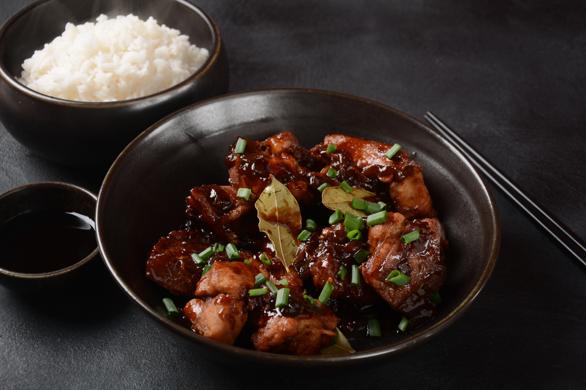 A bowl of food with chopsticks next to a bowl of rice.