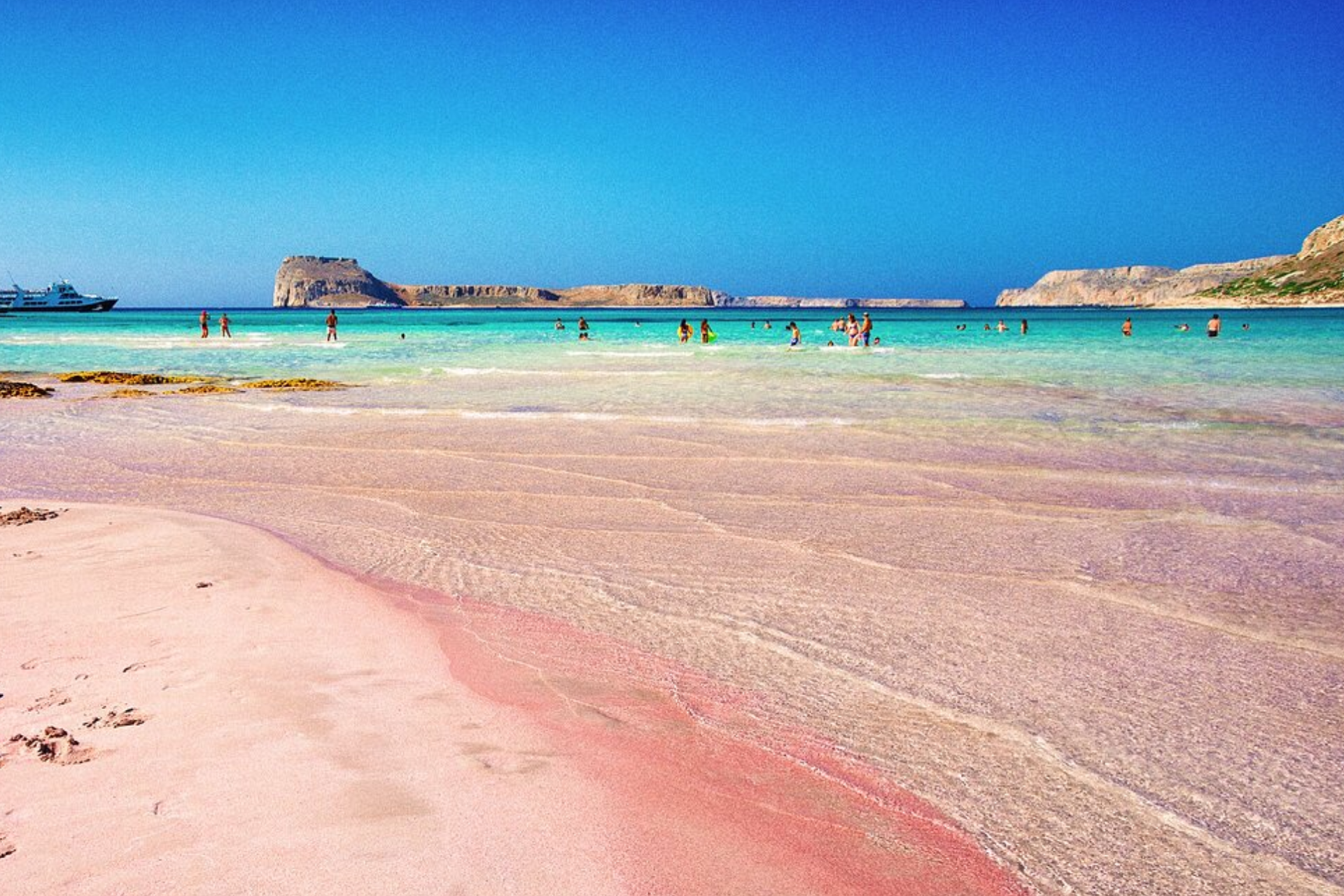 A pink sandy beach with people swimming in the water