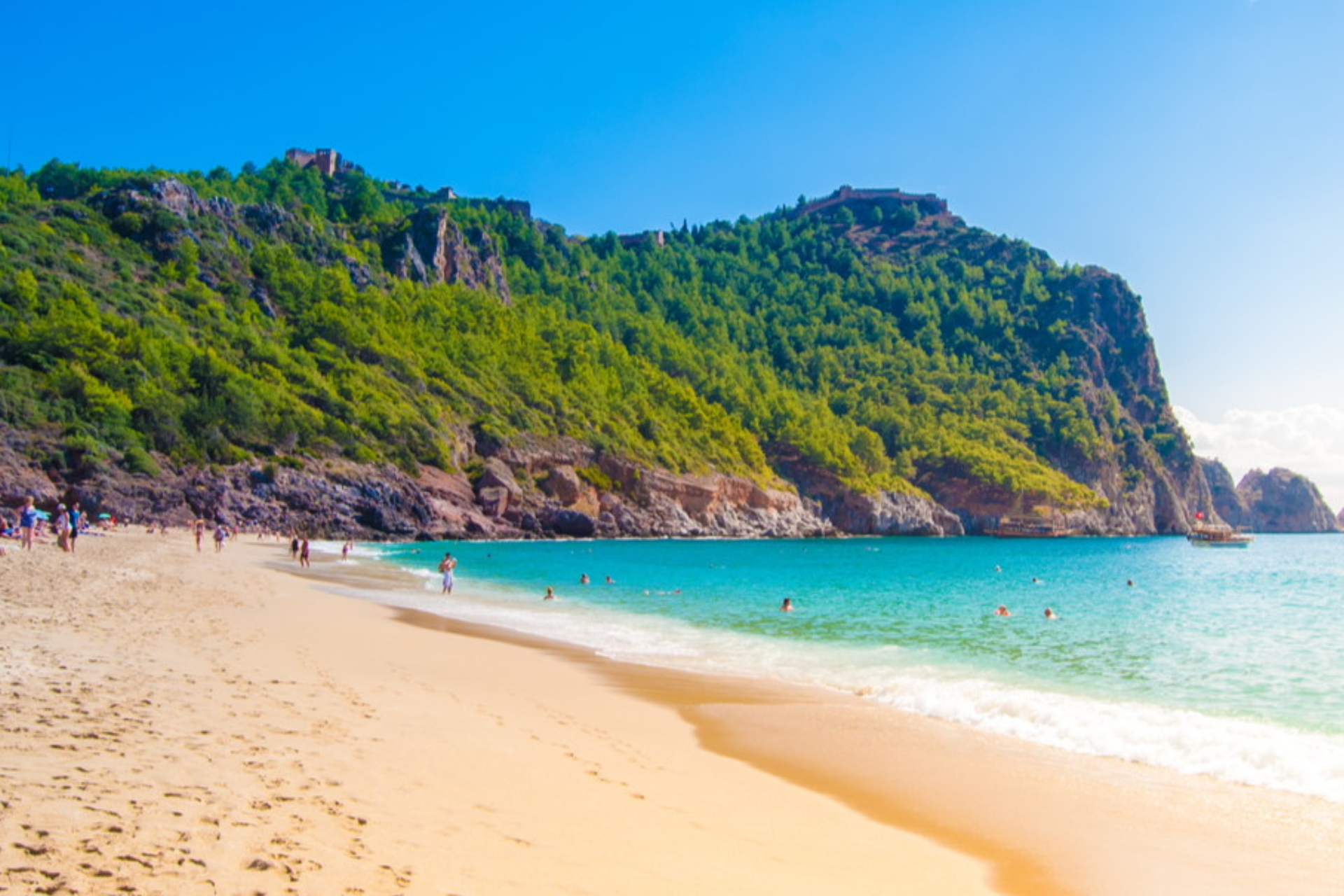 A beach with a mountain in the background and people swimming in the water.