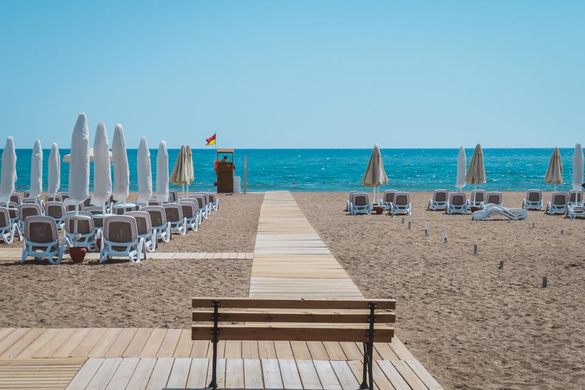 A wooden walkway leading to a beach with chairs and umbrellas.