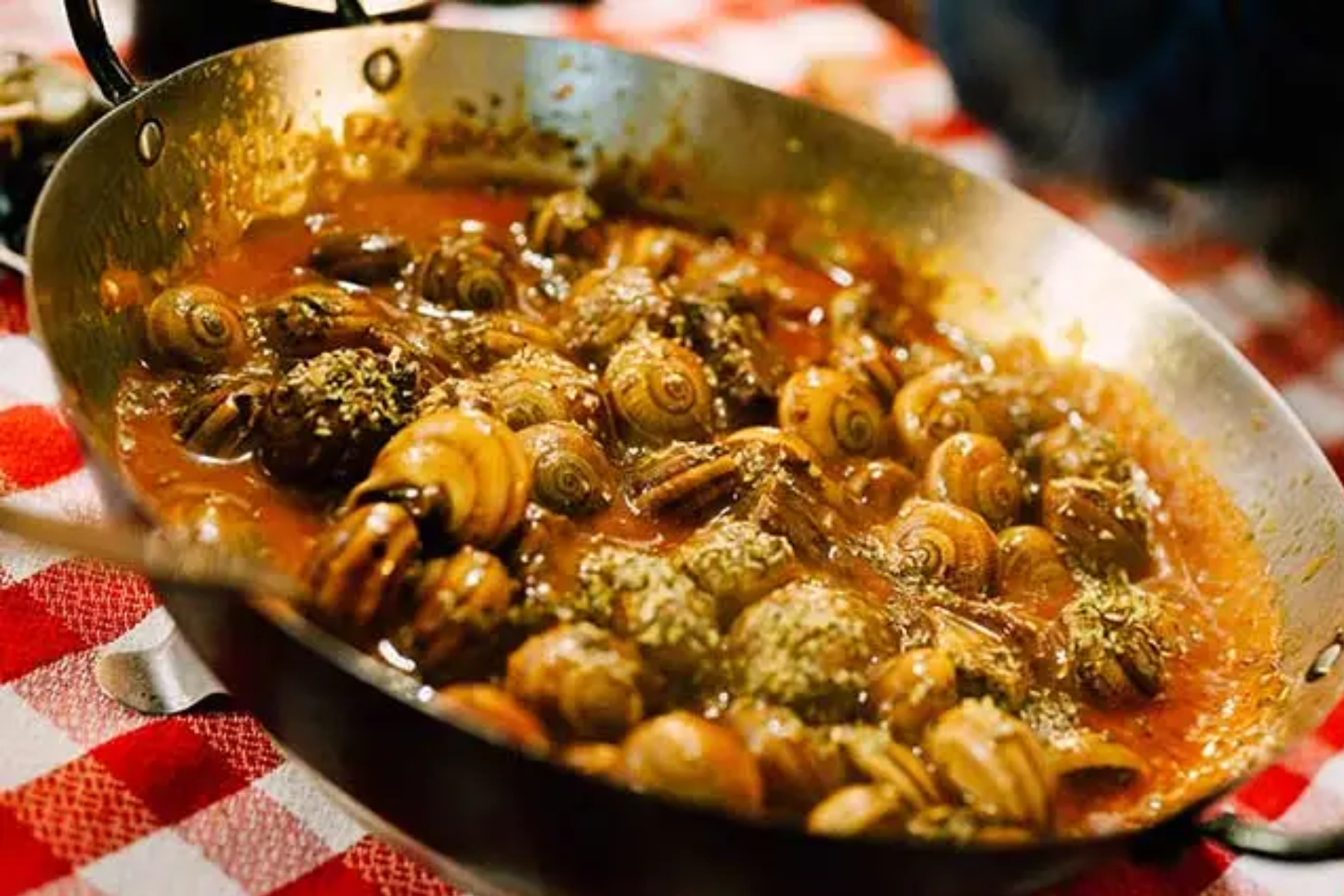 A pan filled with snails in sauce on a checkered table cloth.