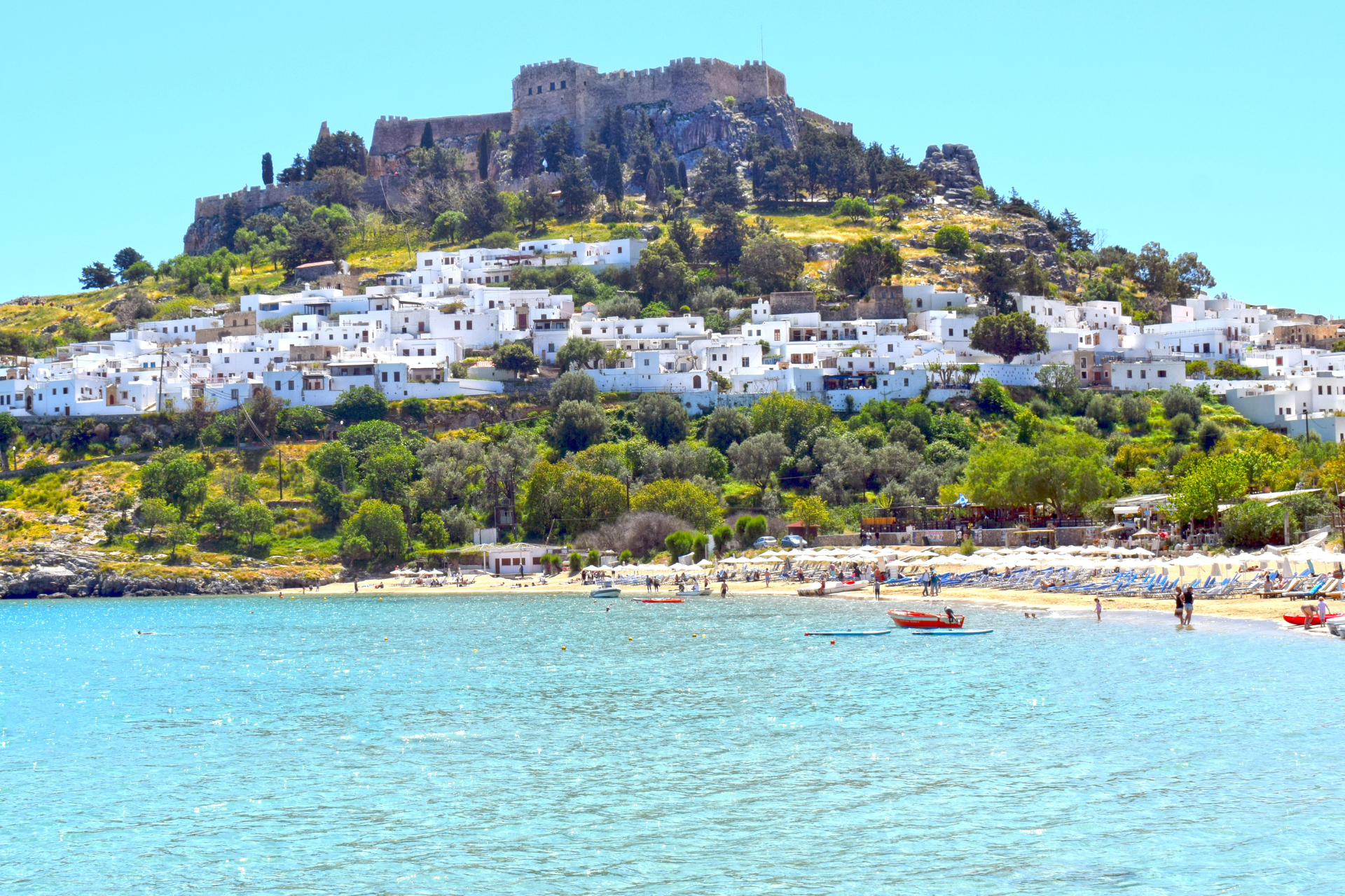 A castle sits on top of a hill overlooking a beach.