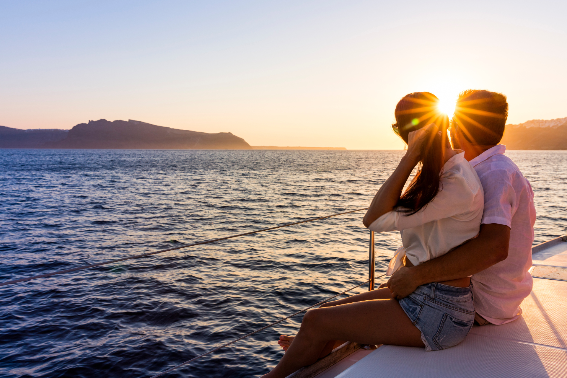 A man and a woman are sitting on the deck of a boat looking at the sunset.