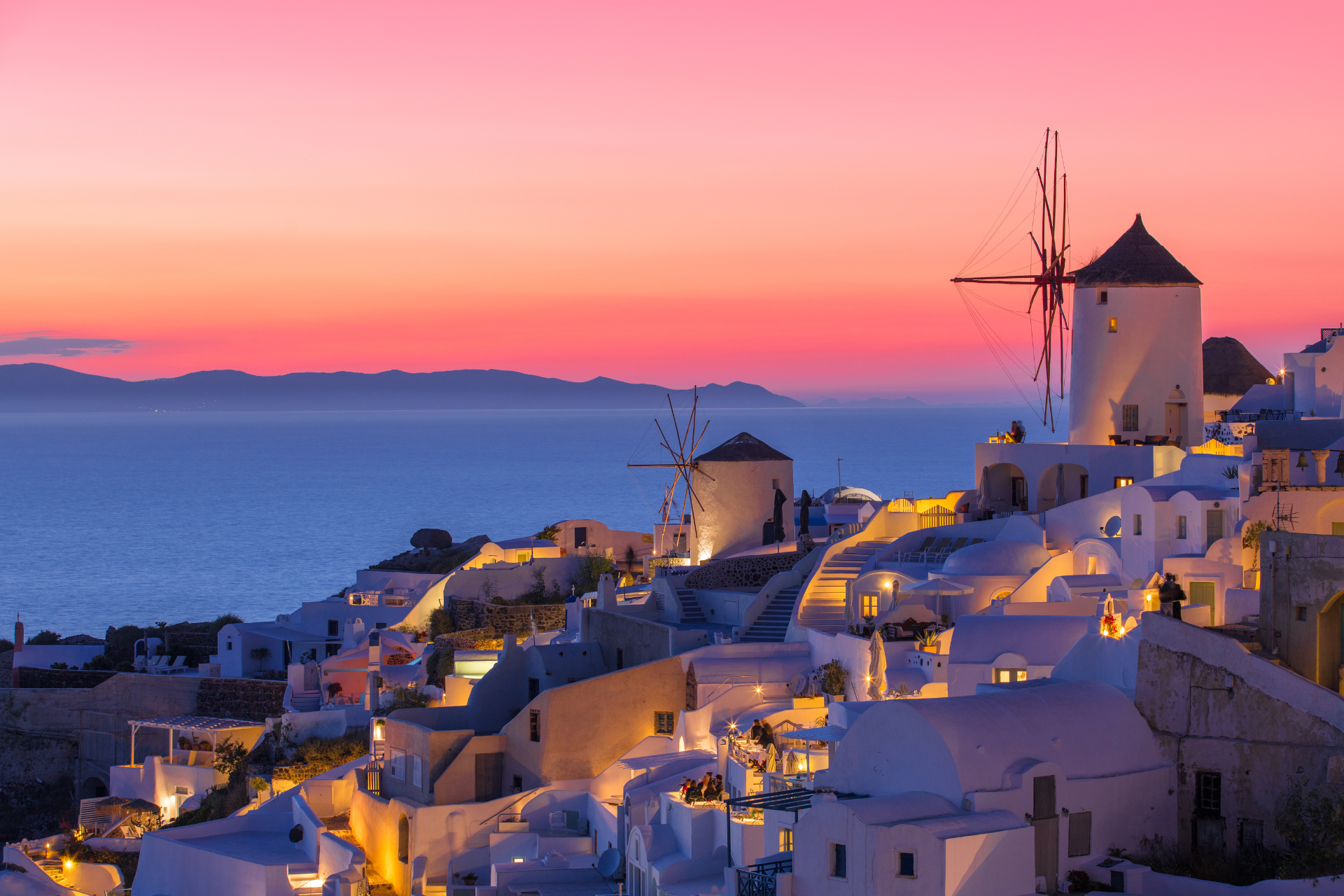 A sunset over a small town with windmills in the foreground and the ocean in the background.