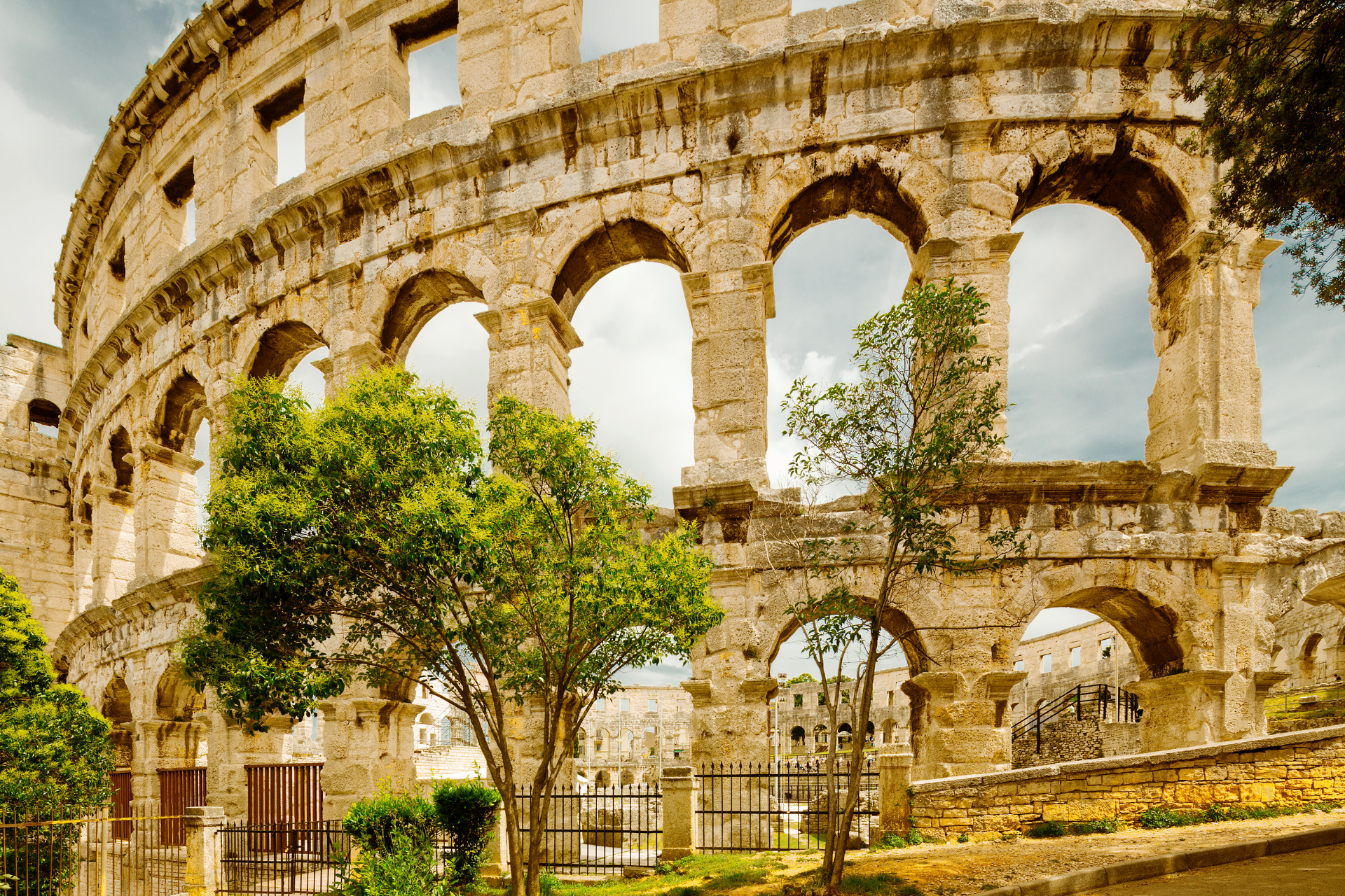 A large stone building with arches and trees in front of it.