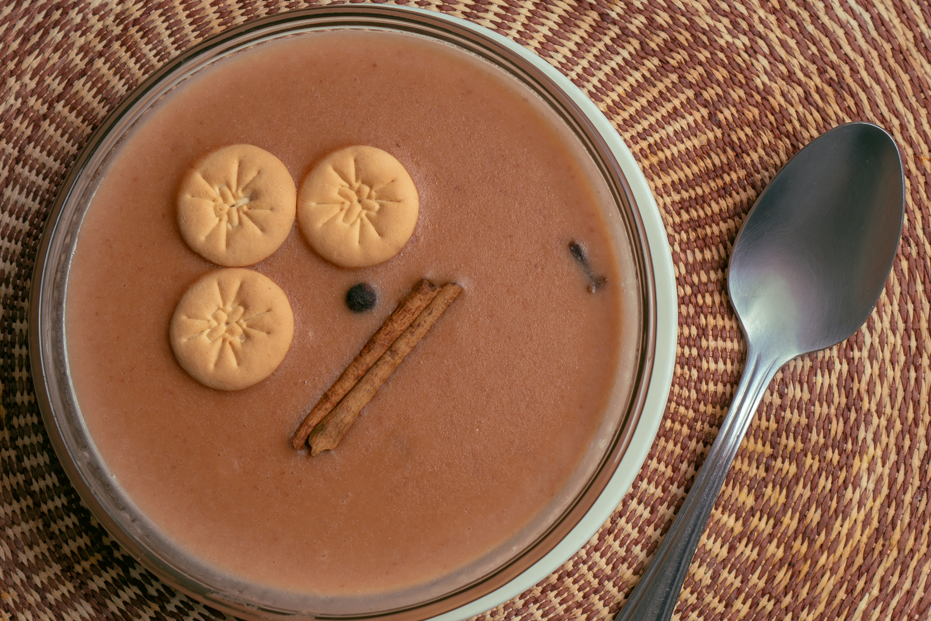 A bowl of soup with cookies and cinnamon sticks next to a spoon