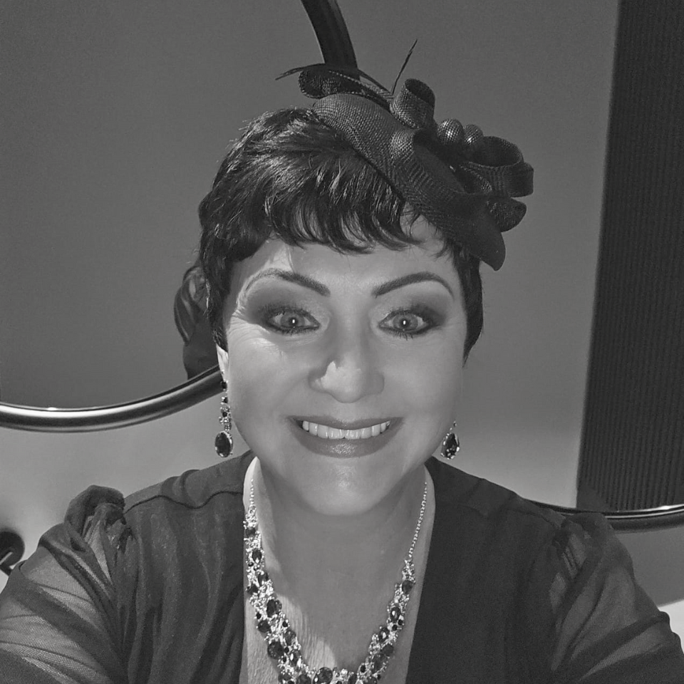 A woman wearing a hat and a necklace smiles in a black and white photo