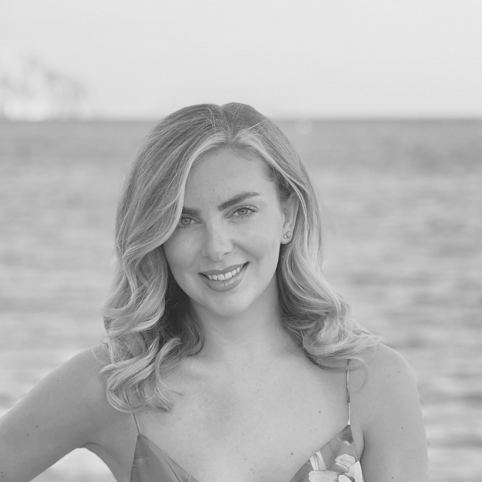 A black and white photo of a woman standing in front of the ocean.