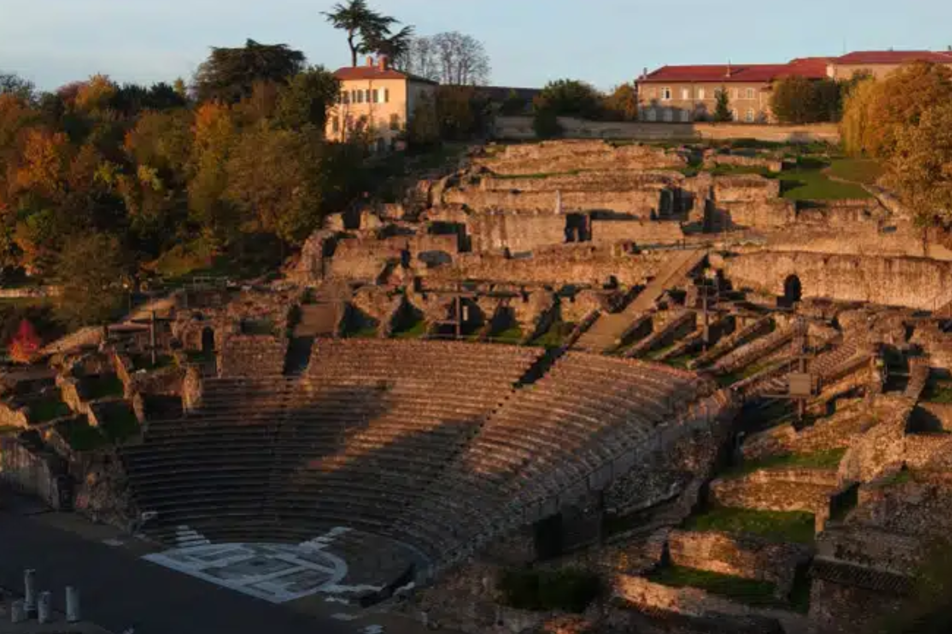 An aerial view of an ancient amphitheater with a building in the background.