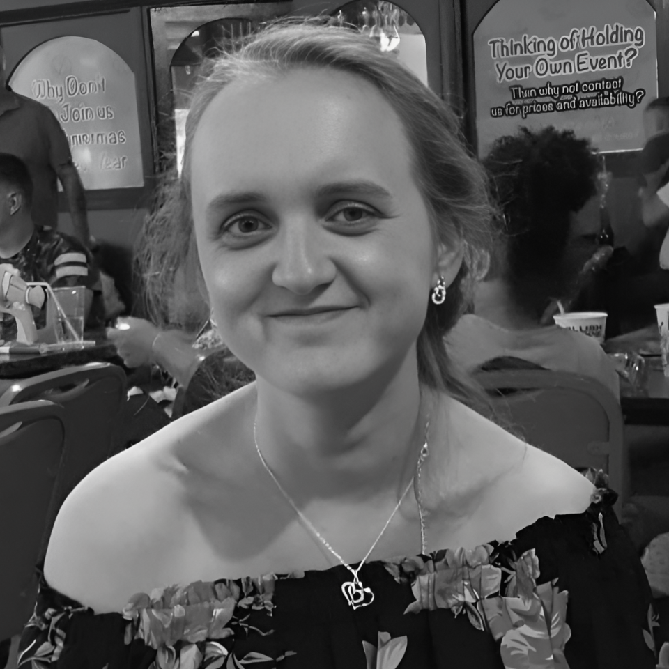 A woman wearing a necklace and earrings is smiling in a black and white photo.