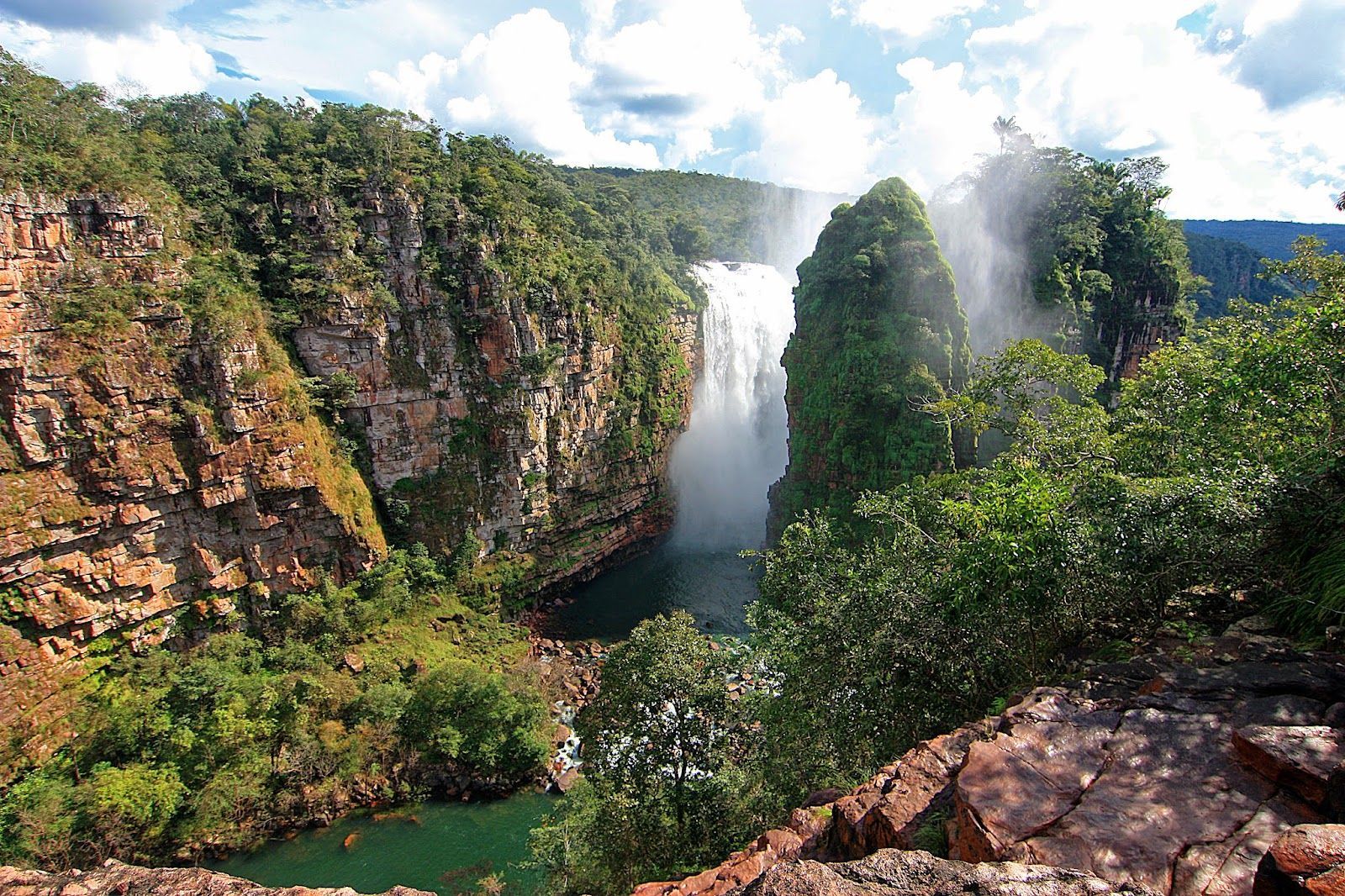 A waterfall in the middle of a canyon surrounded by trees and rocks.