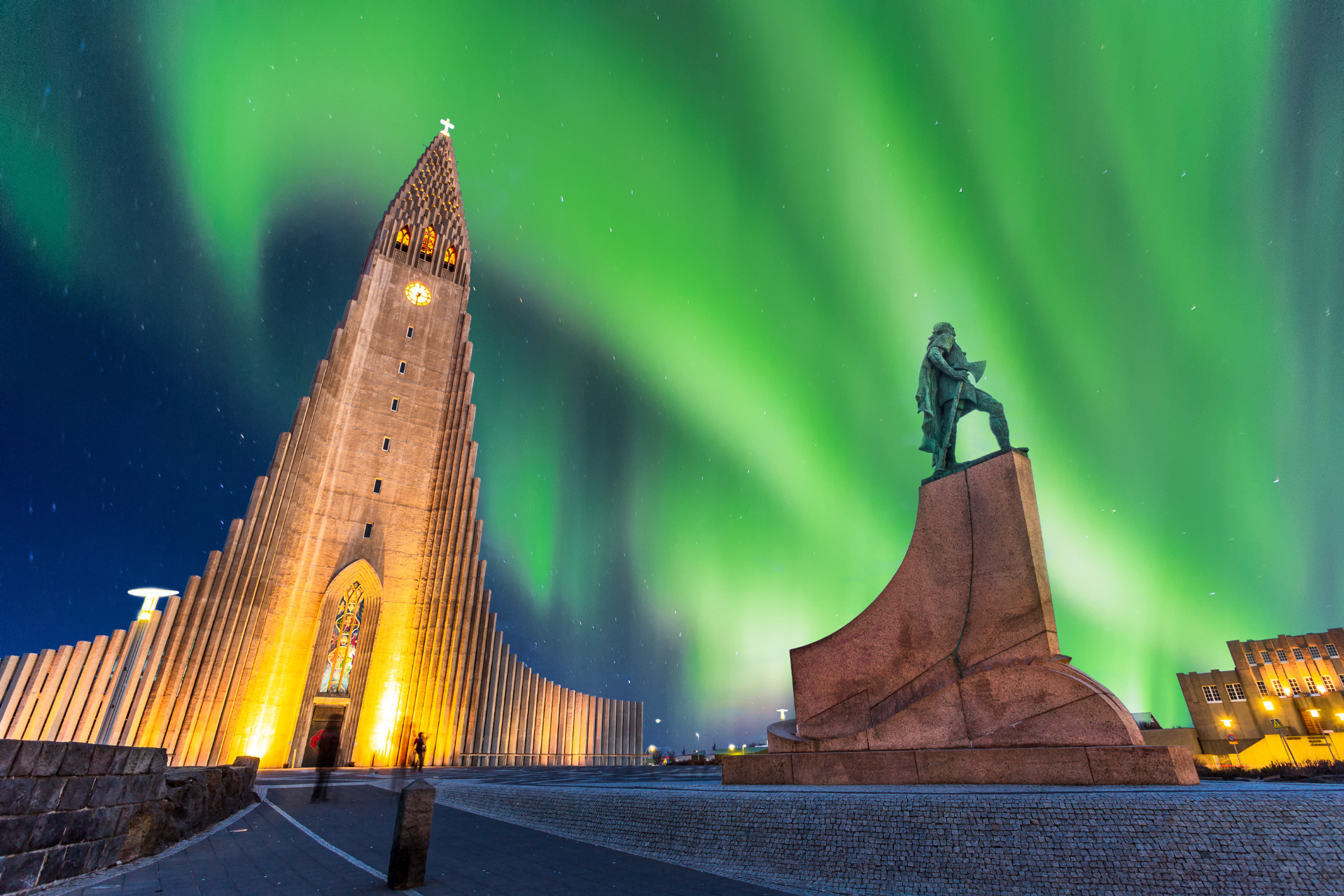 A statue of a man standing in front of a building with the aurora borealis in the background.