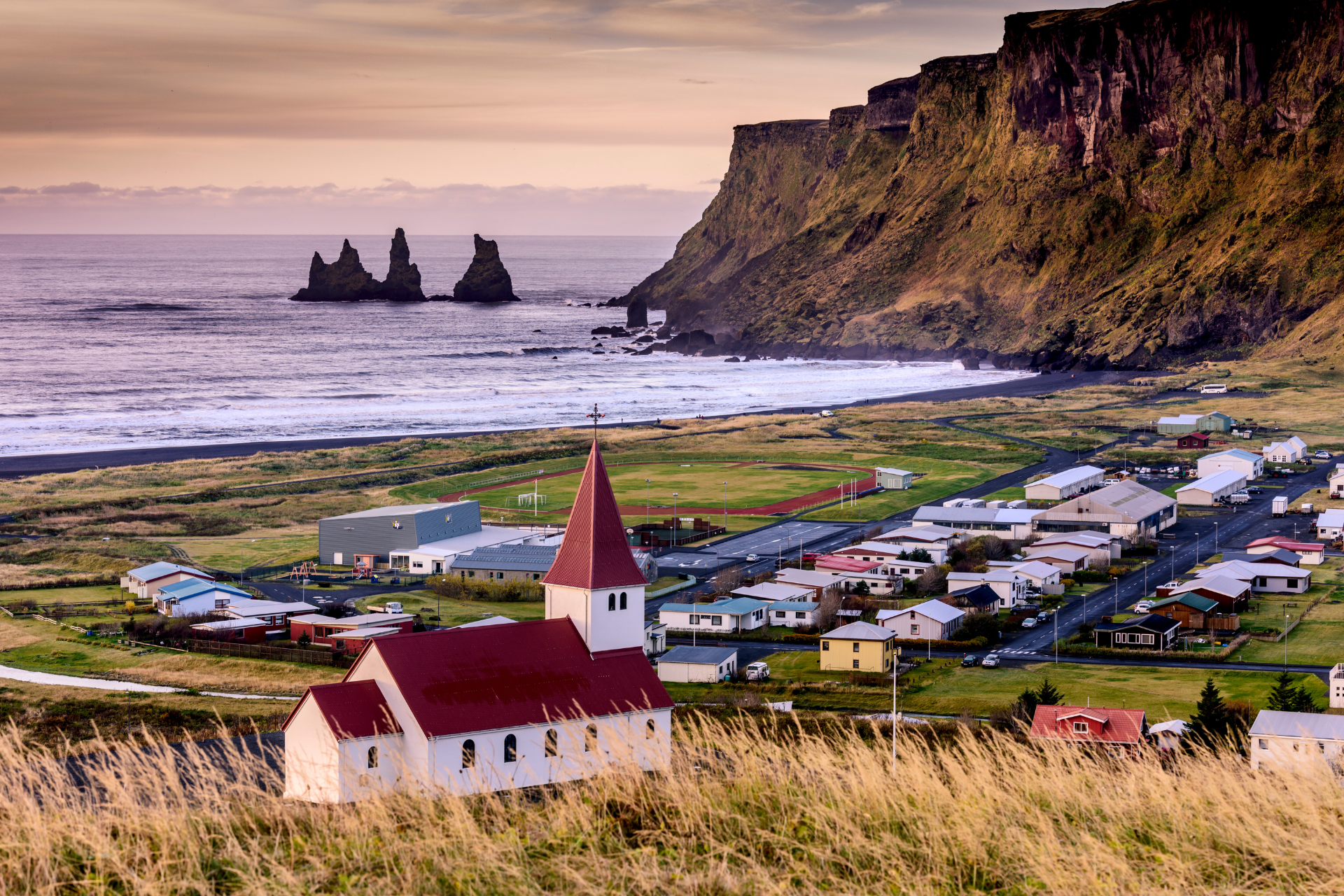 A church with a red roof is sitting on top of a hill near the ocean.