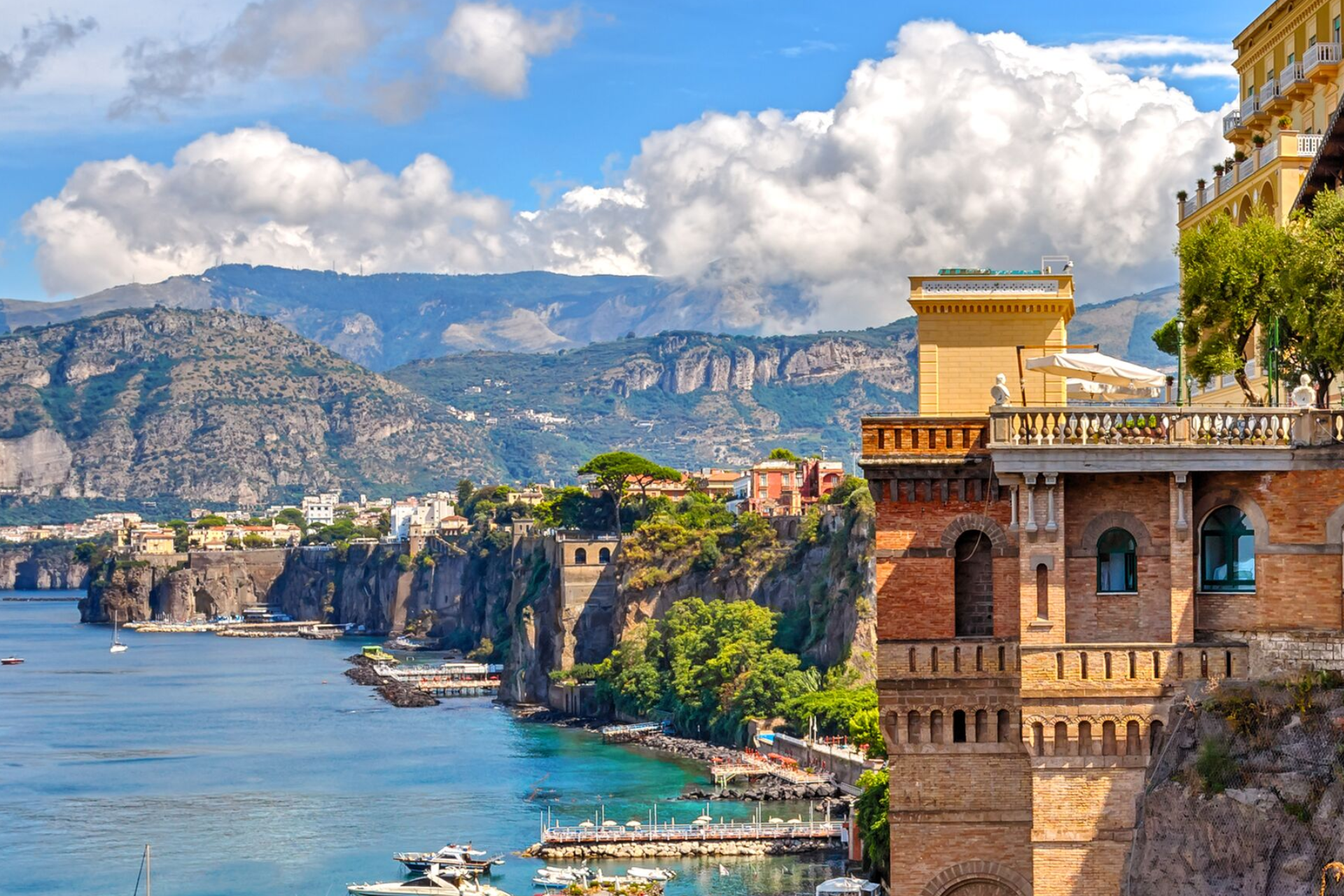 A building on a cliff overlooking a body of water with mountains in the background.