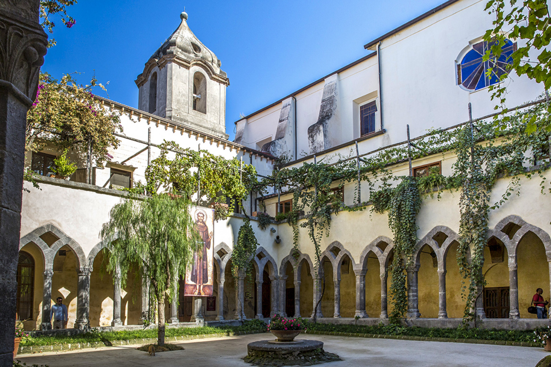 A courtyard with arches and a tower in the background