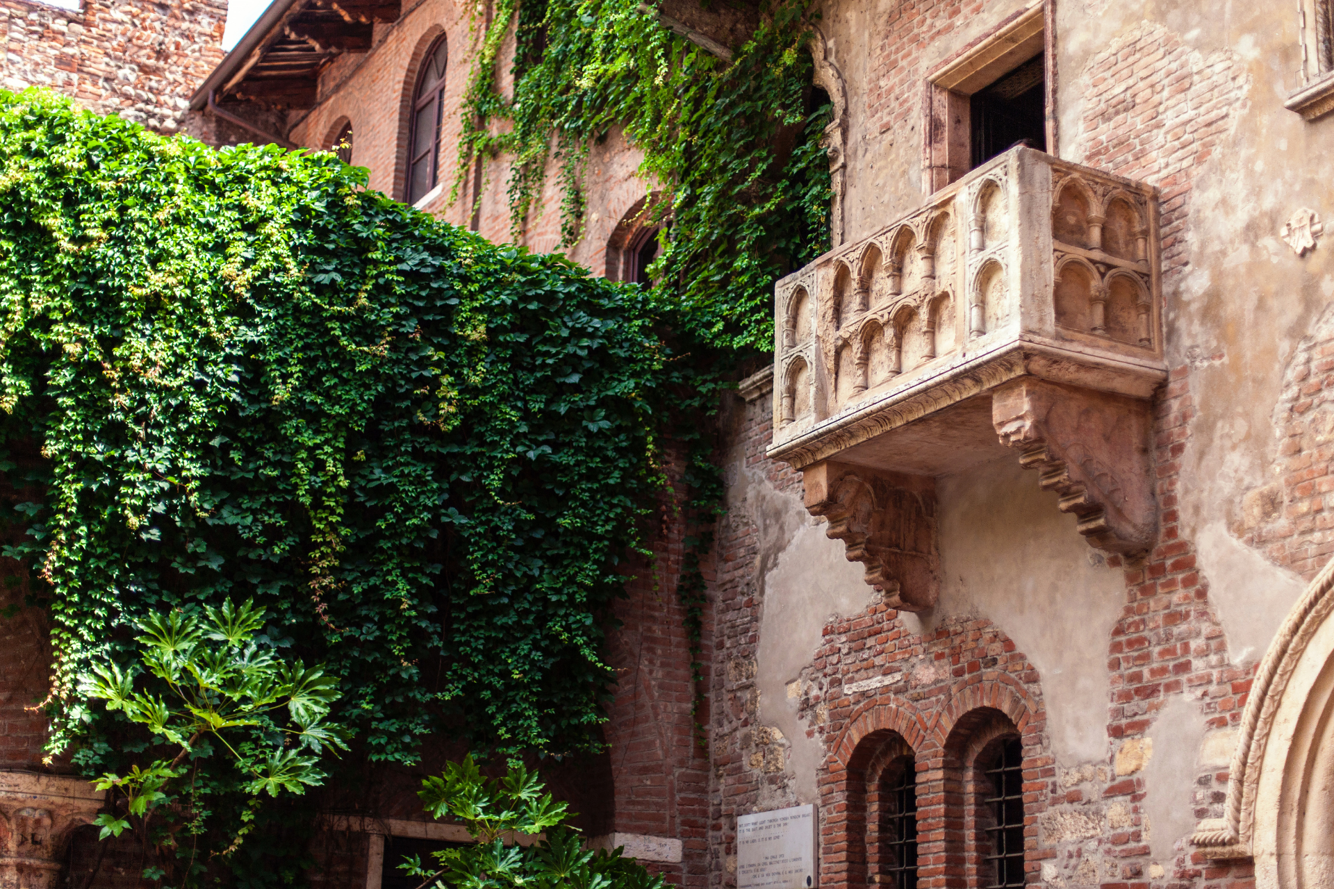 A balcony on the side of a brick building surrounded by ivy.