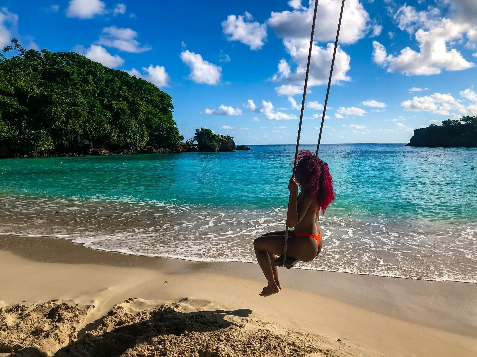 A woman is sitting on a swing on the beach near the ocean.