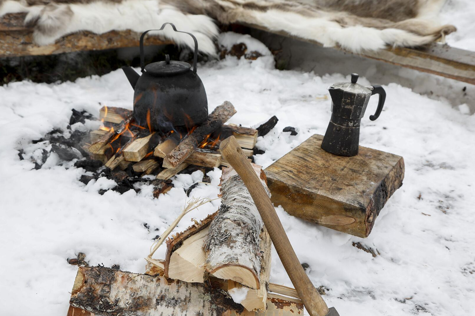 A kettle is cooking over a fire in the snow.