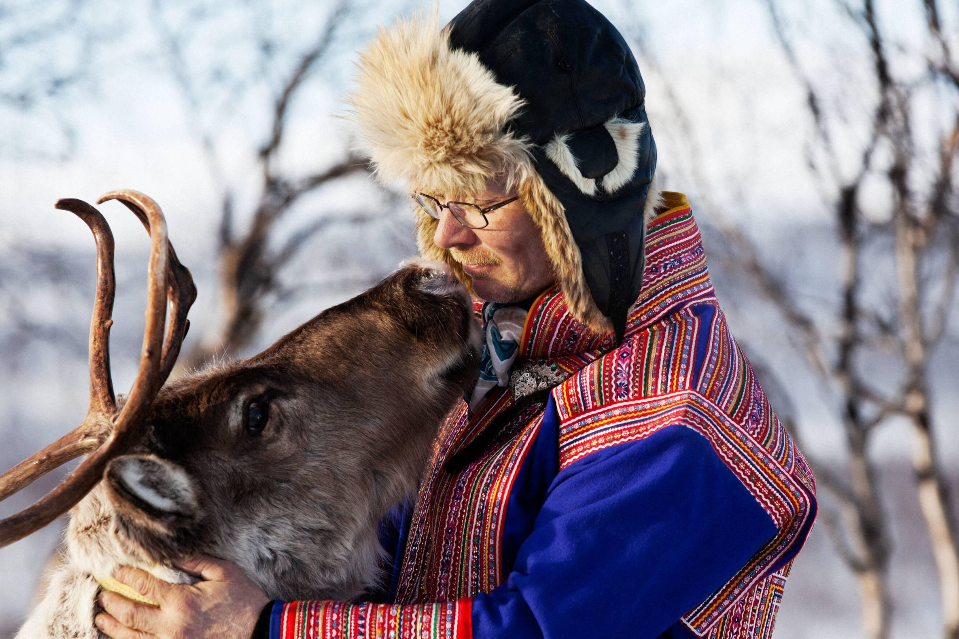 A woman is petting a reindeer in the snow.