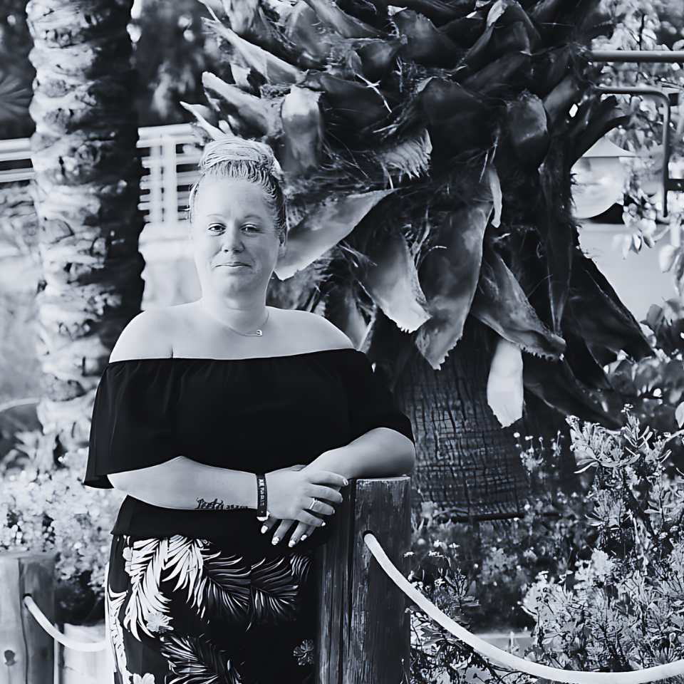 A woman is standing next to a palm tree in a black and white photo.