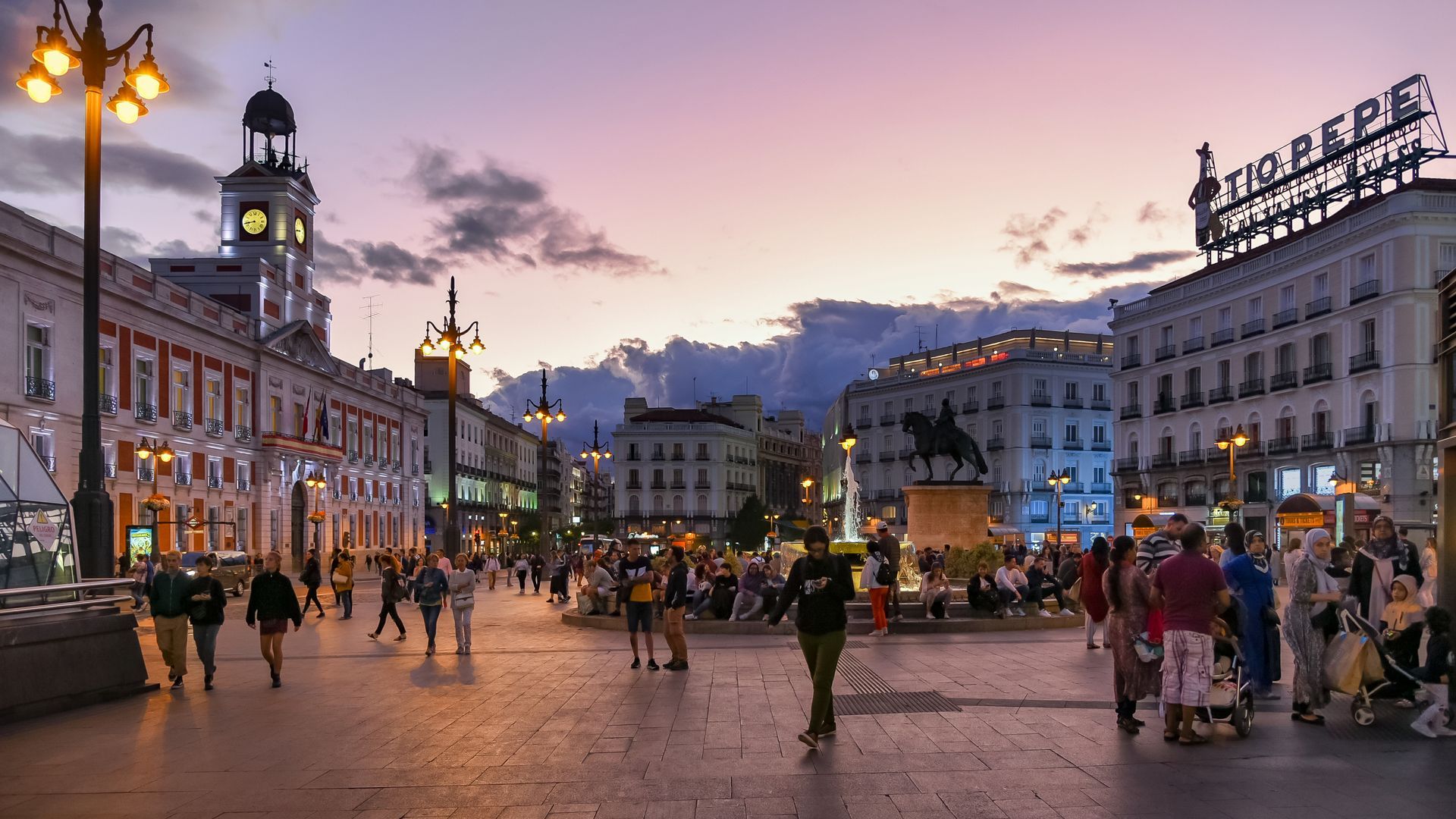 A group of people are walking down a city street at sunset.