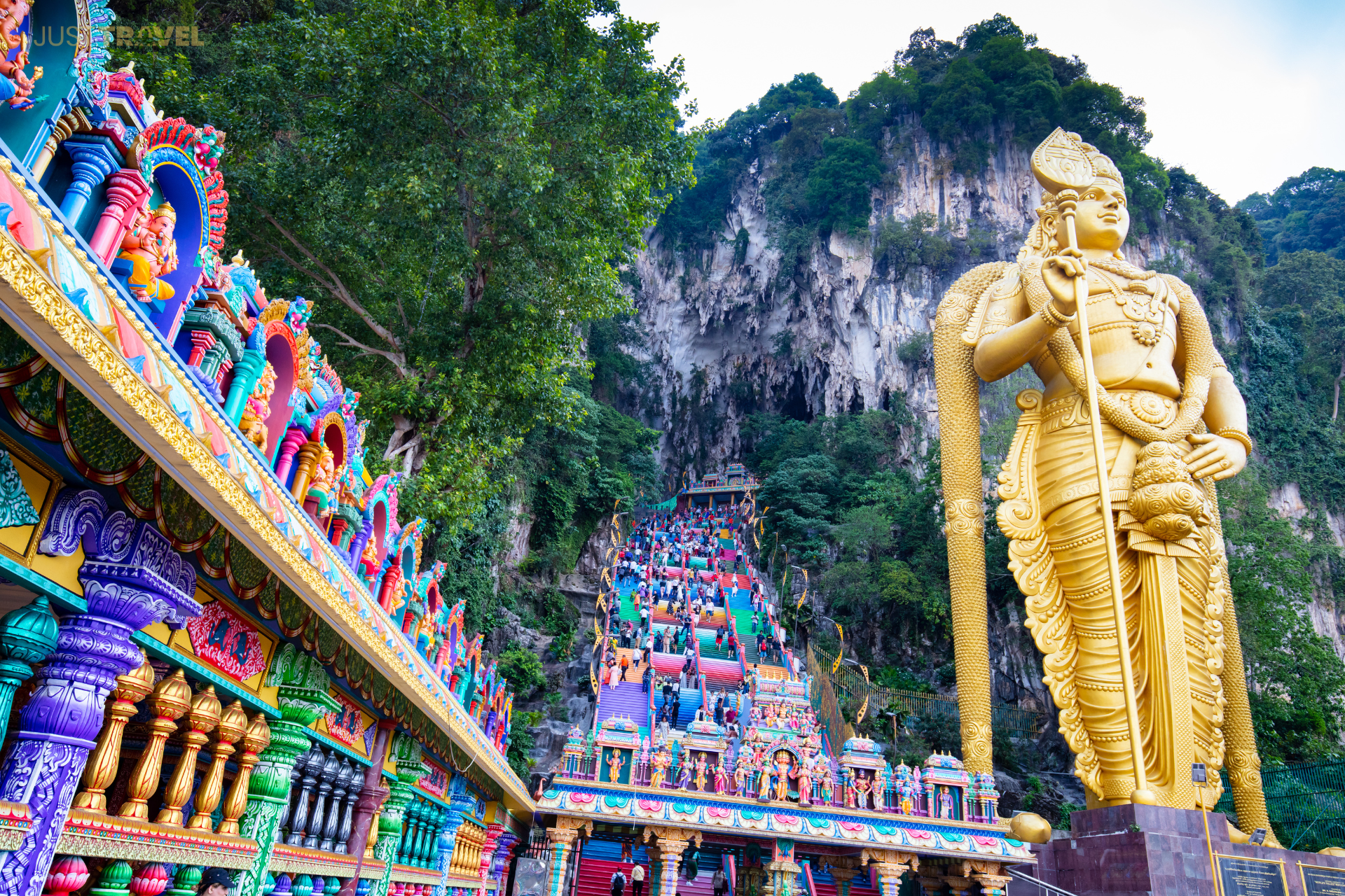 A statue of a man with elephant trunks is in front of a colorful temple.