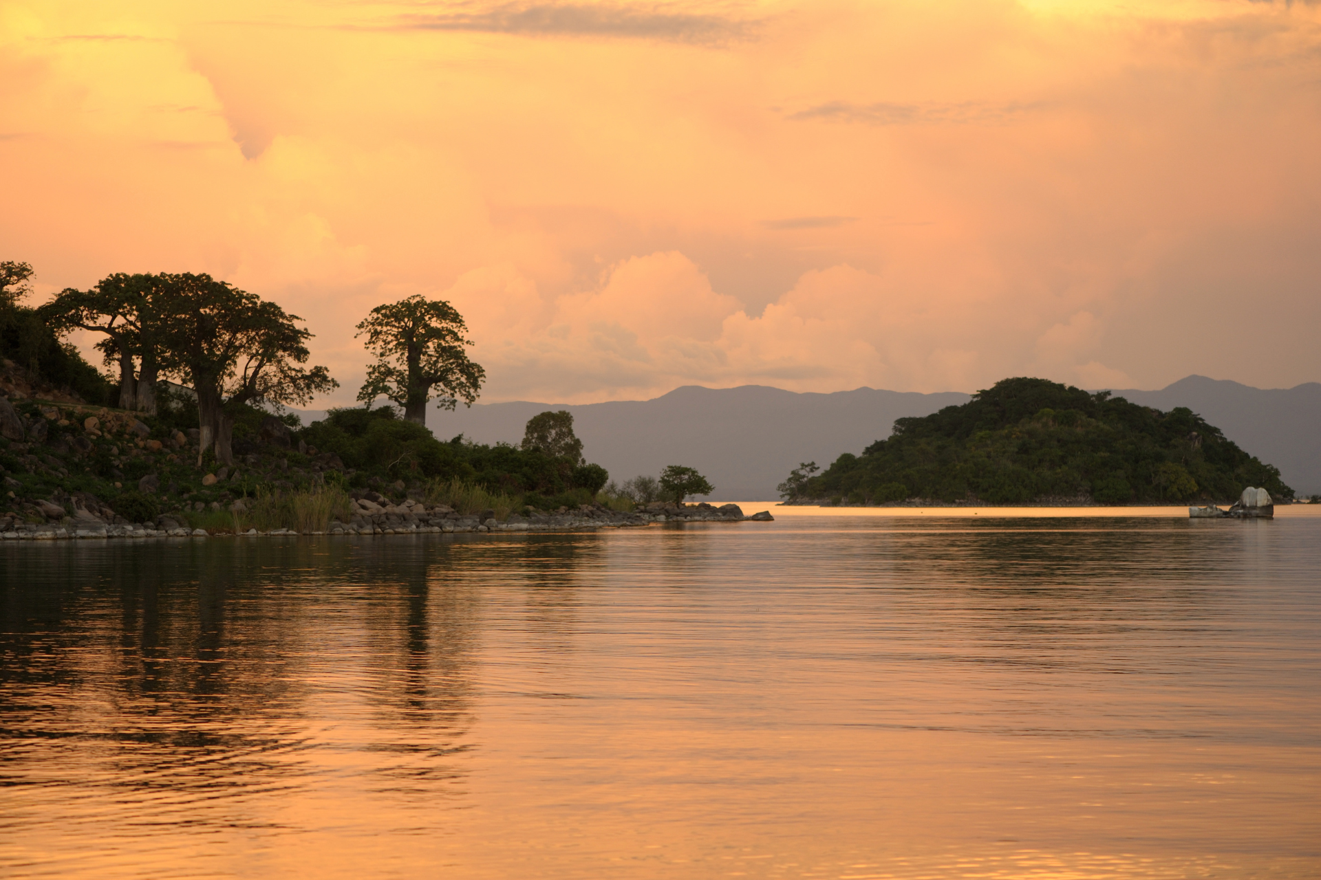 A large body of water with mountains in the background at sunset